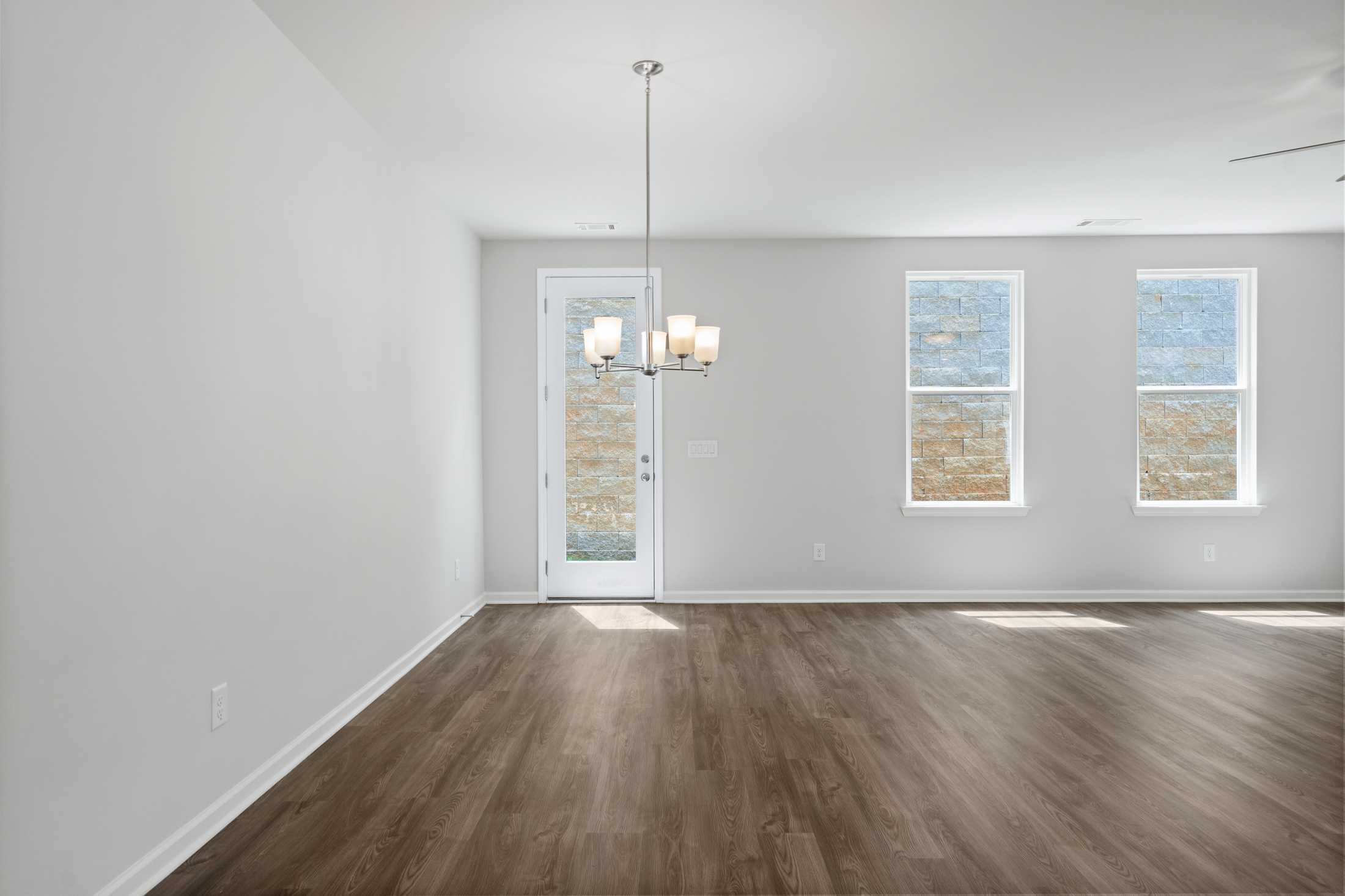 Spacious empty dining room in The Cary A home with hardwood floors, pendant chandelier, glass door, and large windows