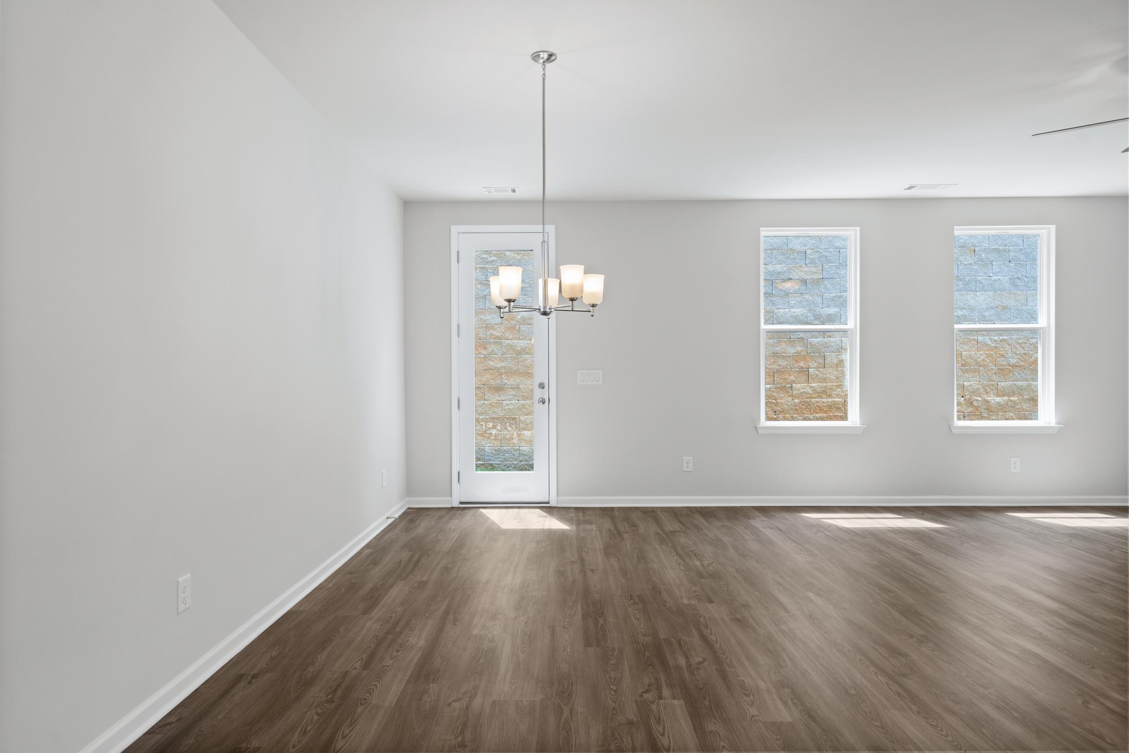 Spacious empty dining room in The Cary A home with hardwood floors, pendant chandelier, glass door, and large windows