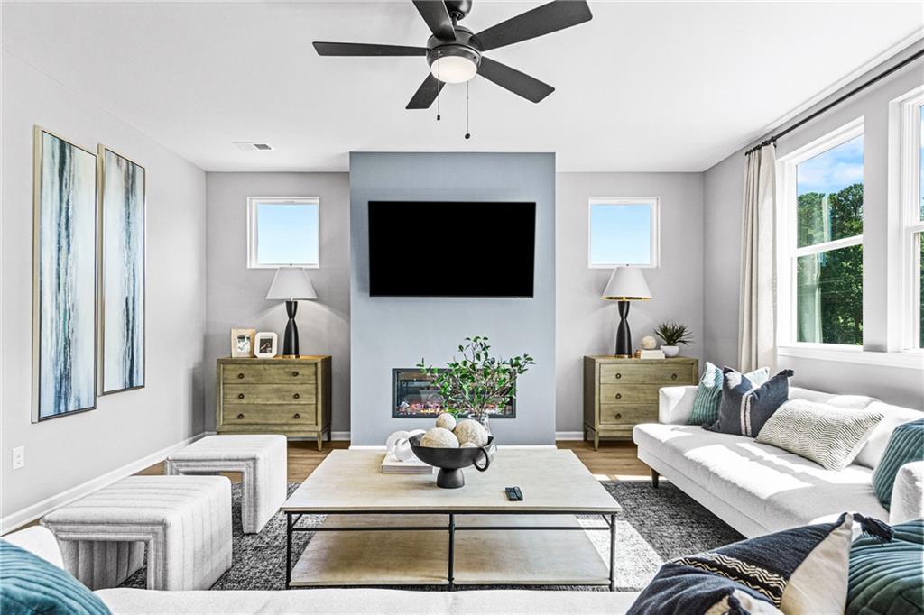 Modern living room with fireplace, flat-screen TV, and ceiling fan in The Hickory A floor plan at Wehunt Meadows, Hoschton.