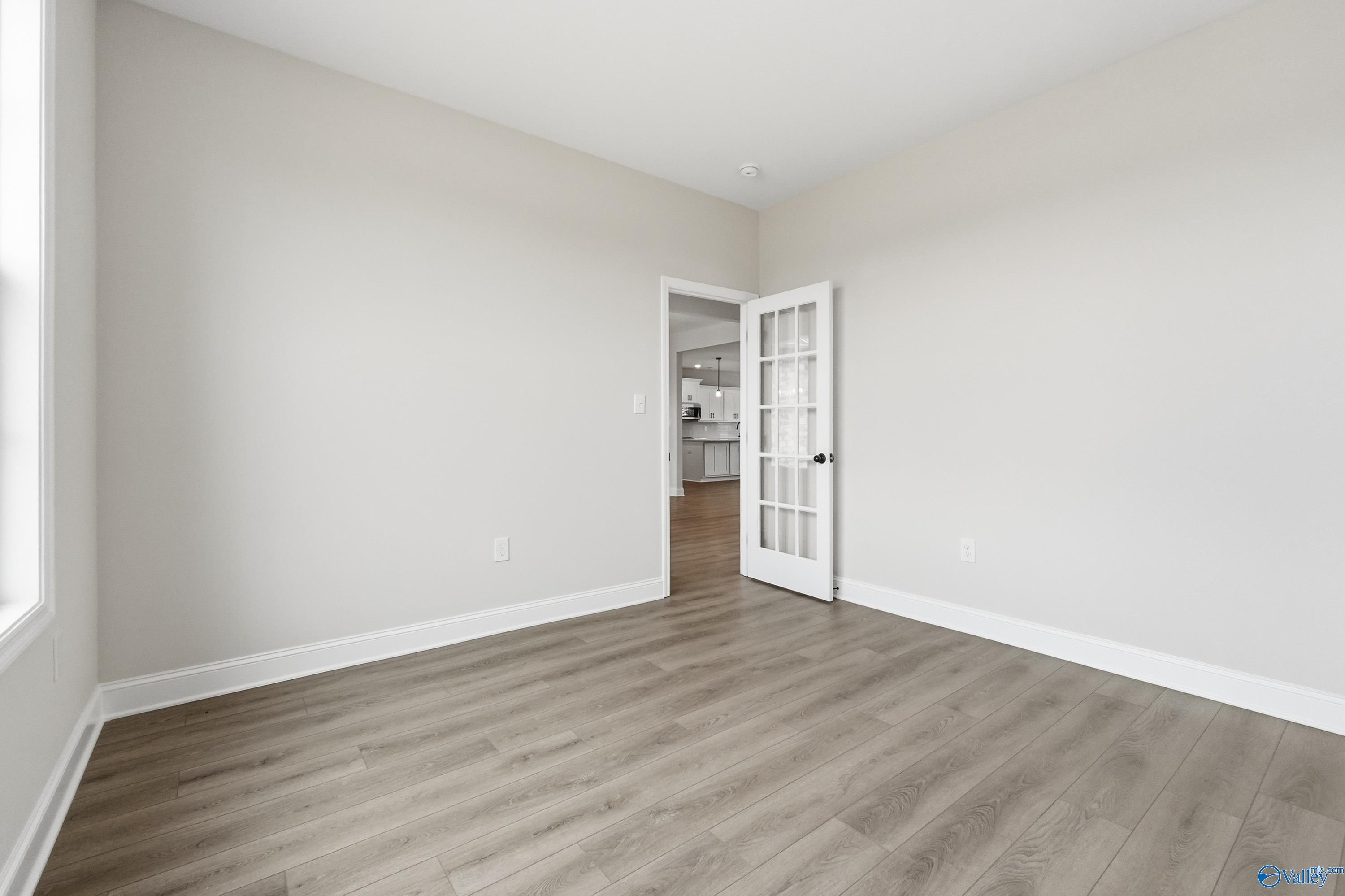 Bright bedroom with light gray walls, luxury vinyl plank flooring, and French doors to kitchen in Davidson Homes The Finleigh, Meridianville, Alabama