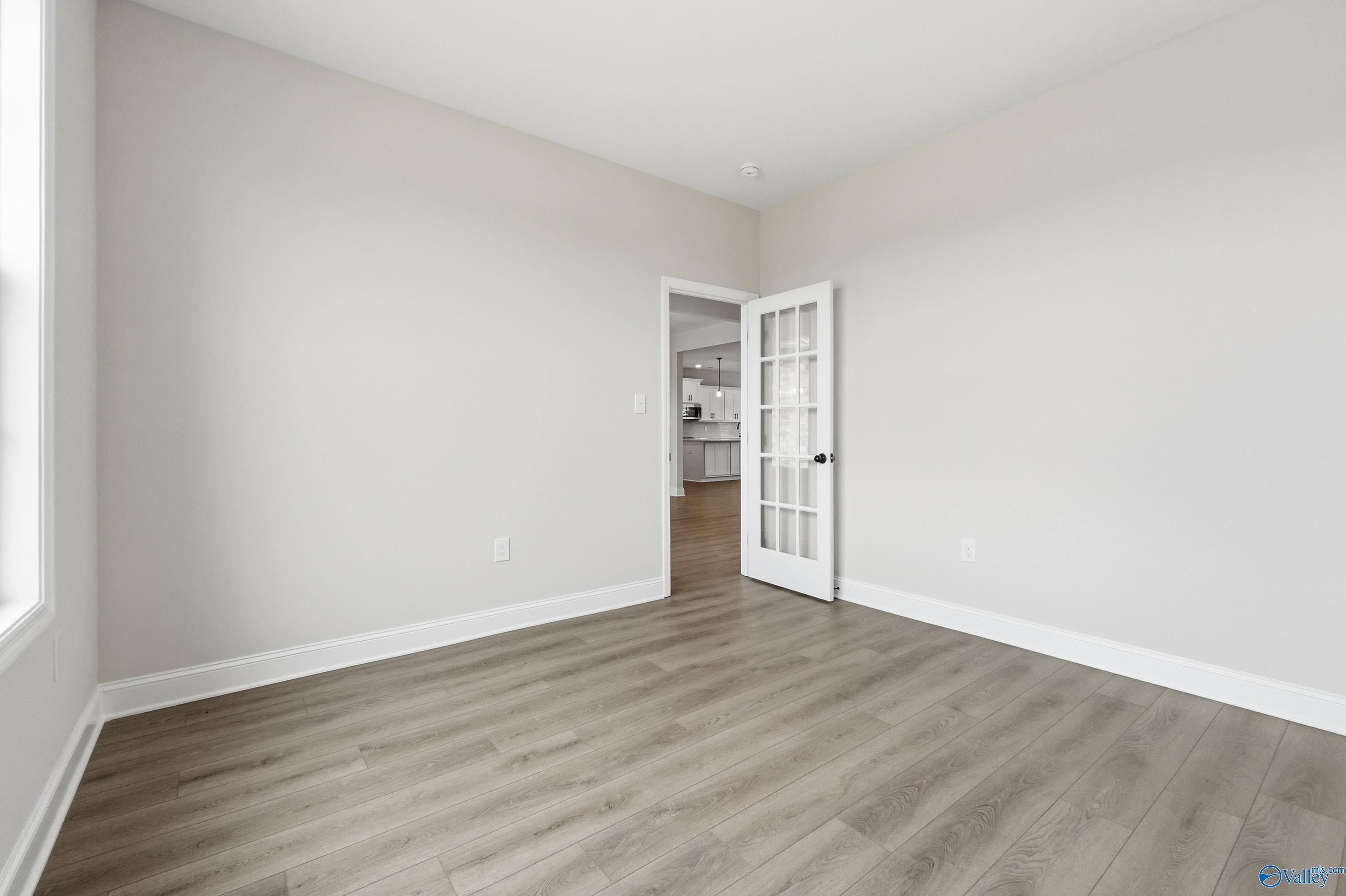 Bright bedroom with light gray walls, luxury vinyl plank flooring, and French doors to kitchen in Davidson Homes The Finleigh, Meridianville, Alabama