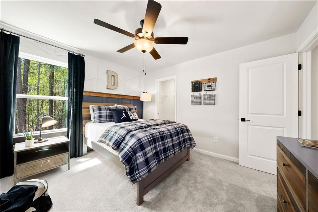 Cozy boy's bedroom with navy plaid bedding, wooden headboard, ceiling fan, and tree-view window in The Willow B by Davidson Homes, Riverwood, Dallas, Georgia