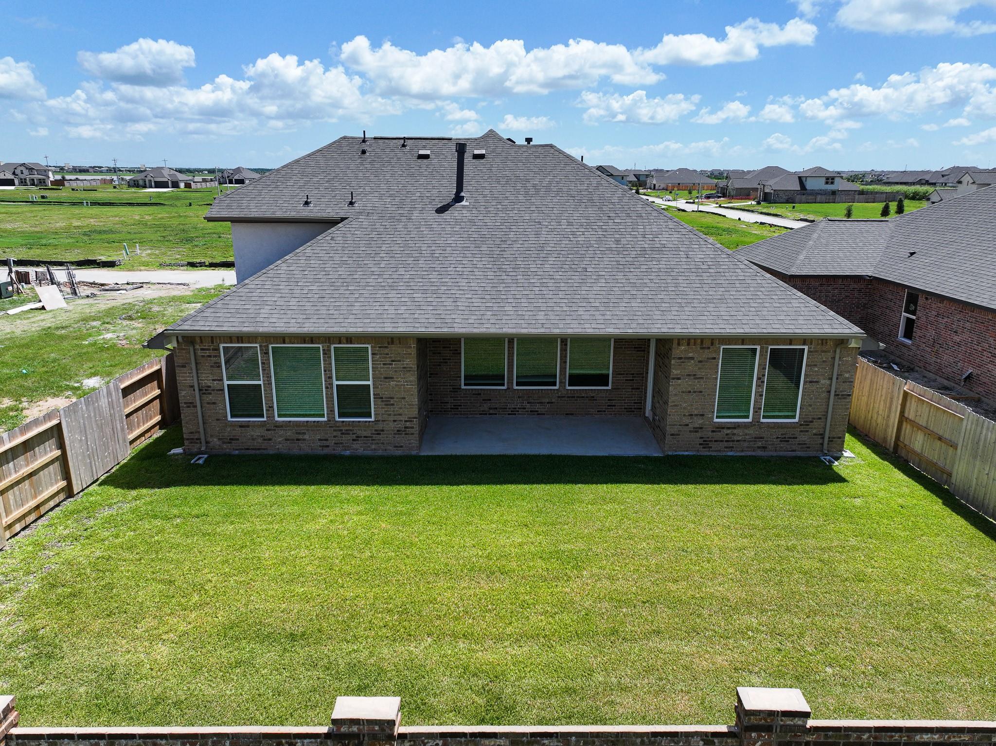 Rear view of Davidson Homes Edward C: single-story brick home with covered patio, fenced grassy backyard in Lago Mar, Texas City, Texas