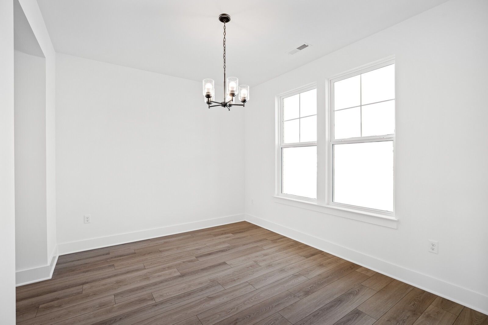 Bright dining room with modern chandelier and wood-look flooring in The Willow C floor plan at Woods Crossing, Gallatin.