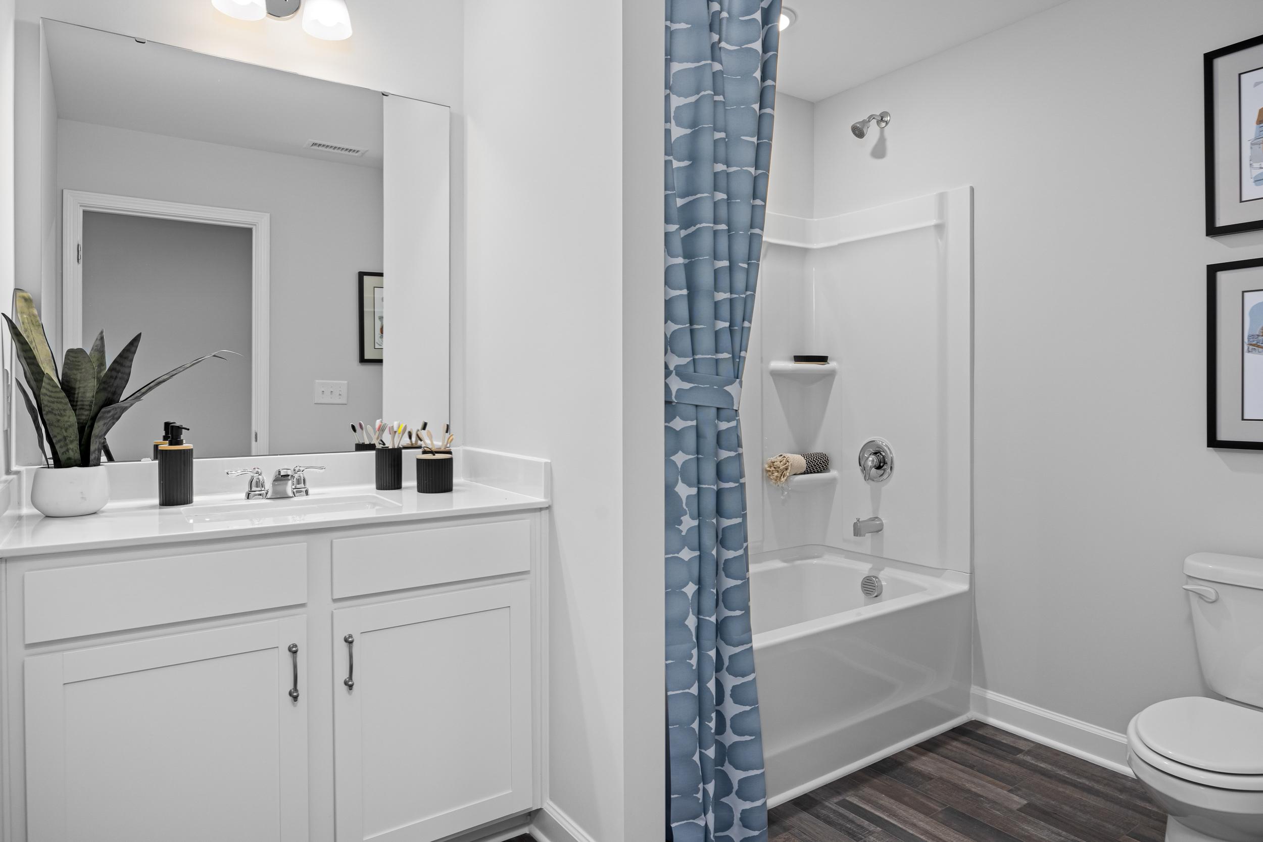 Spacious master bathroom in The Magnolia A featuring white double vanity, tub-shower combo with blue curtains, and modern fixtures