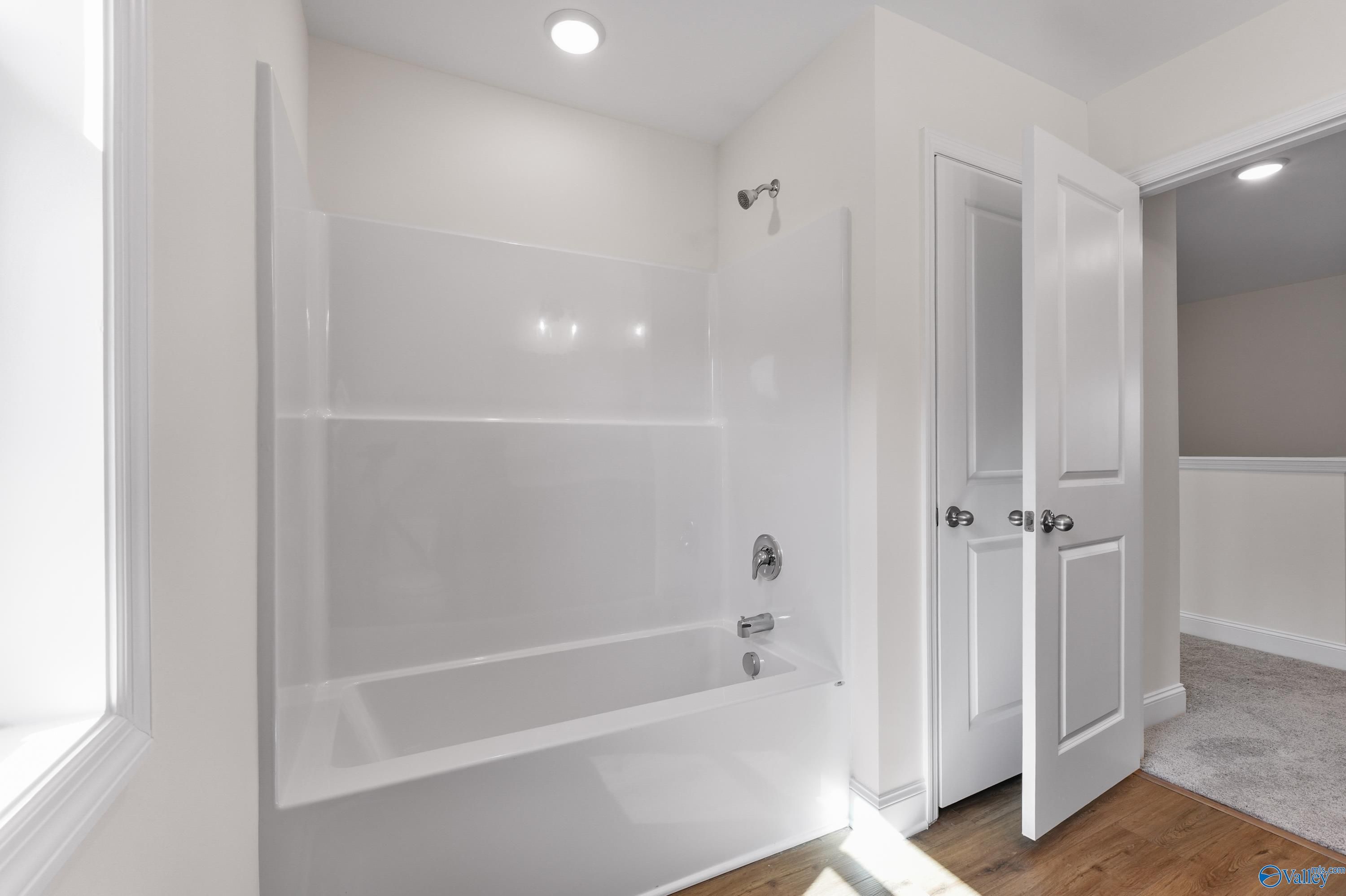Bright white bathroom with bathtub, glass shower, and open closet doors in Davidson Homes The Shelby A, Athens, Alabama