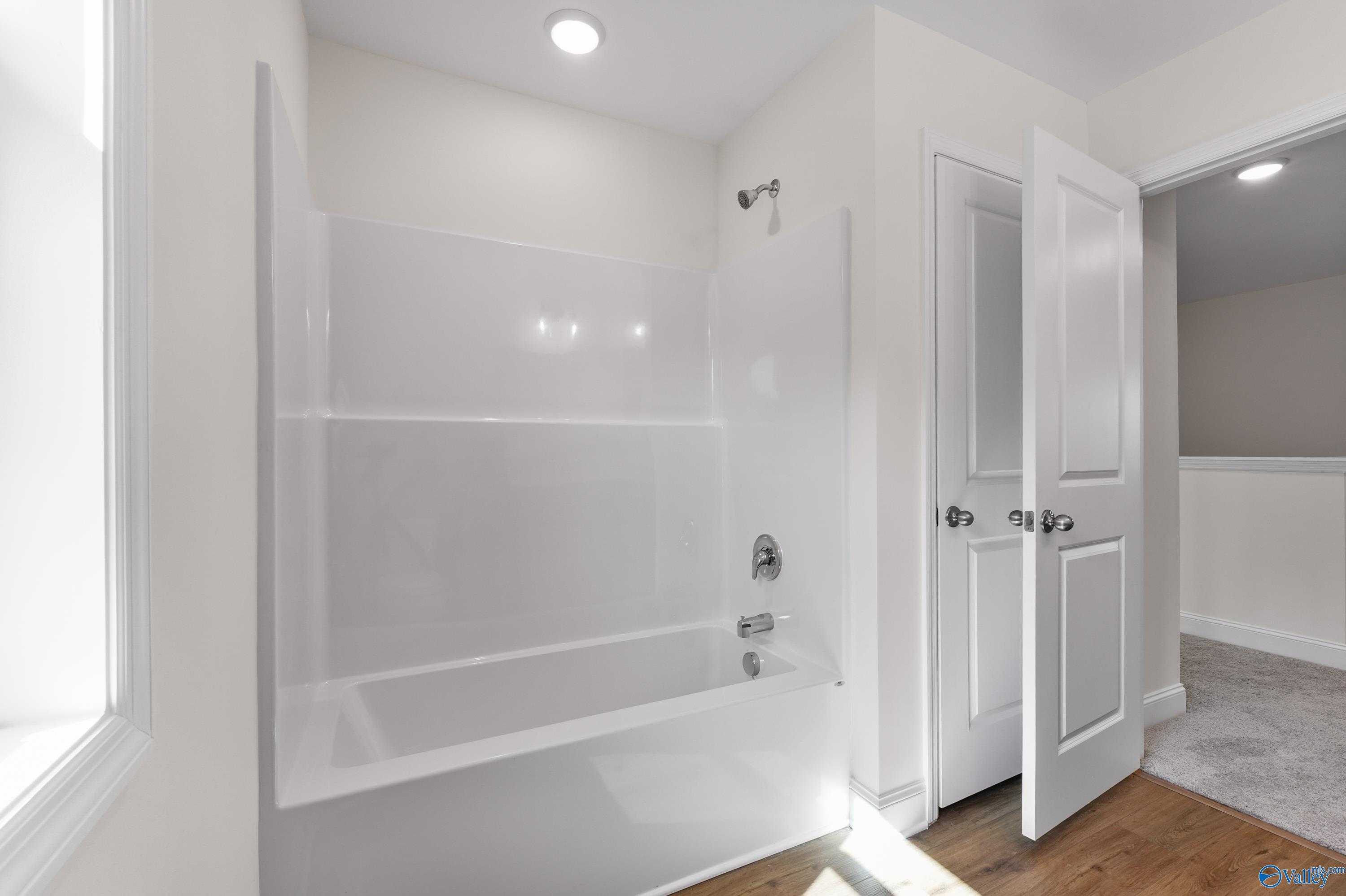 Bright white secondary bathroom with tub-shower combo and glass enclosure in Davidson Homes The Shelby A, Athens, AL