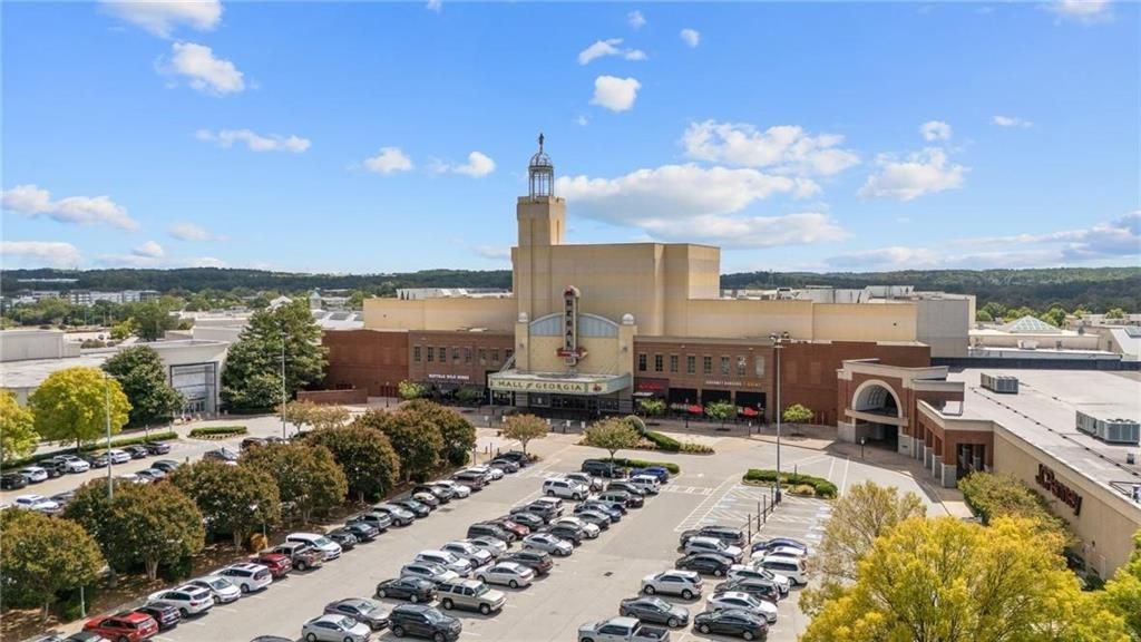 Aerial view of beige brick movie theater with tower marquee, retail shops, parking lots, and autumn trees near Melody Lakeside Estates, Buford, Georgia