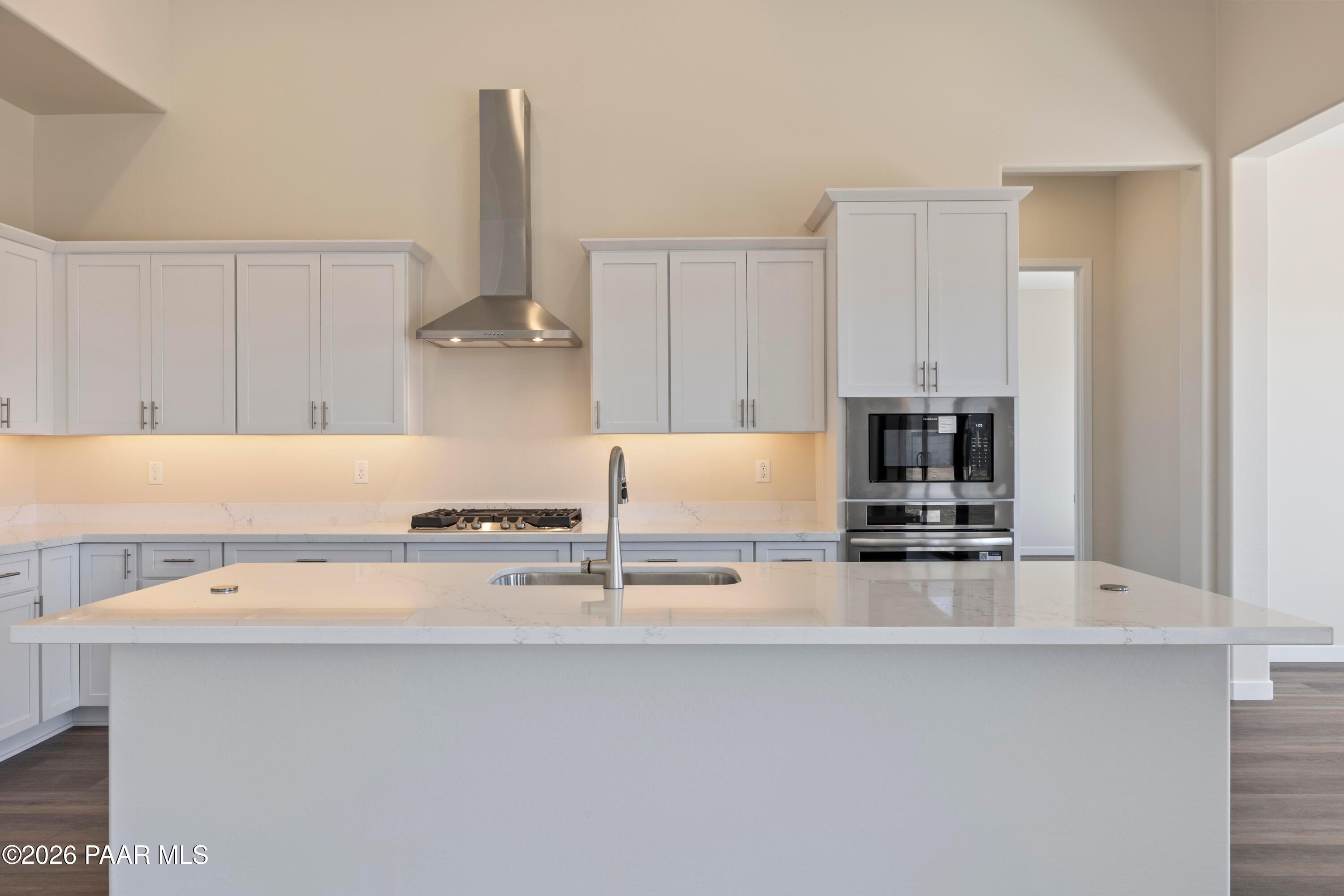Modern white kitchen island with sink, stainless steel oven, and gas cooktop in Davidson Homes The Soleil E, Prescott, Arizona