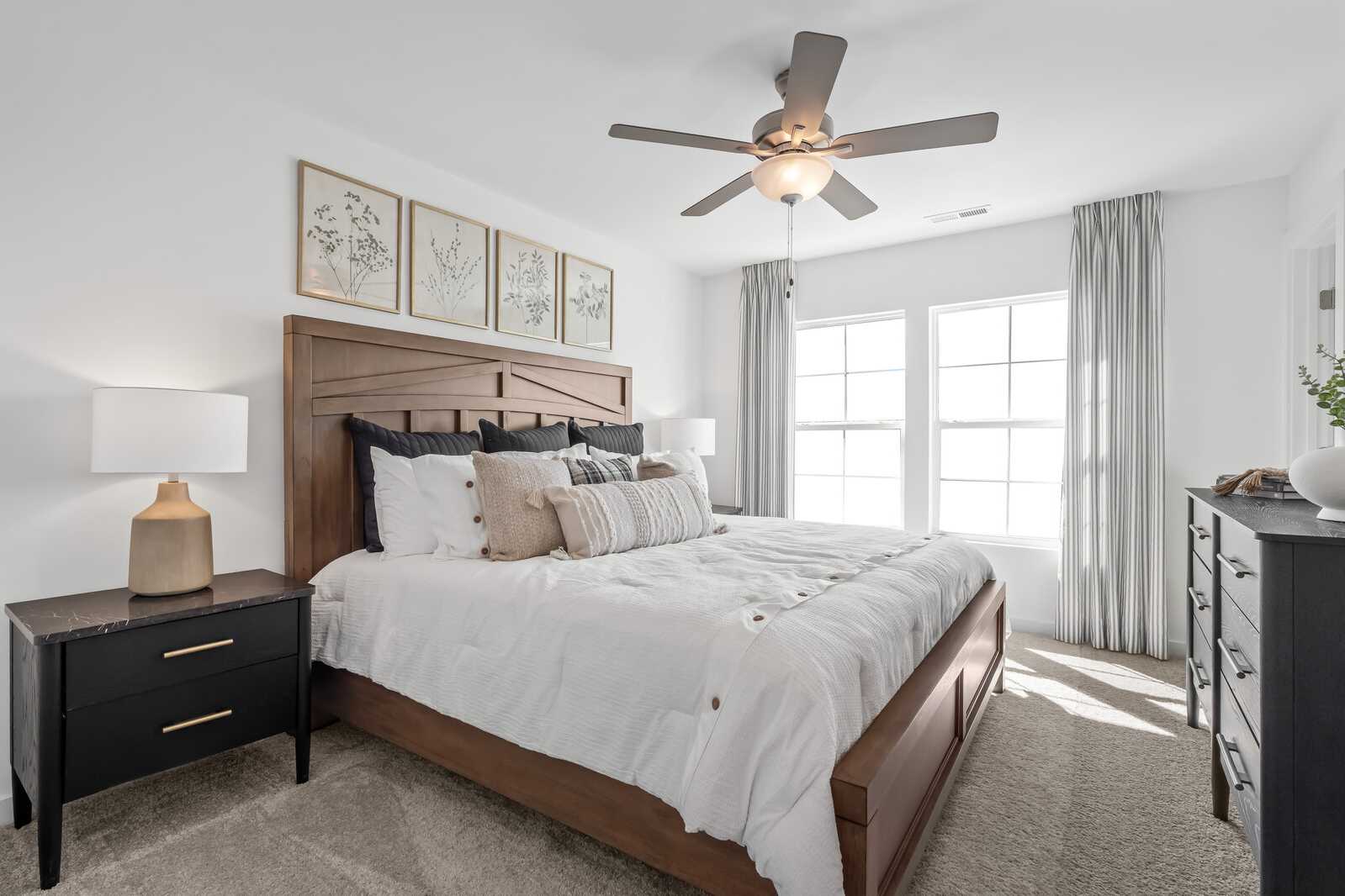 Primary bedroom at The Towns at Red River in Gallatin TN with wooden king bed, neutral bedding, ceiling fan, and large windows