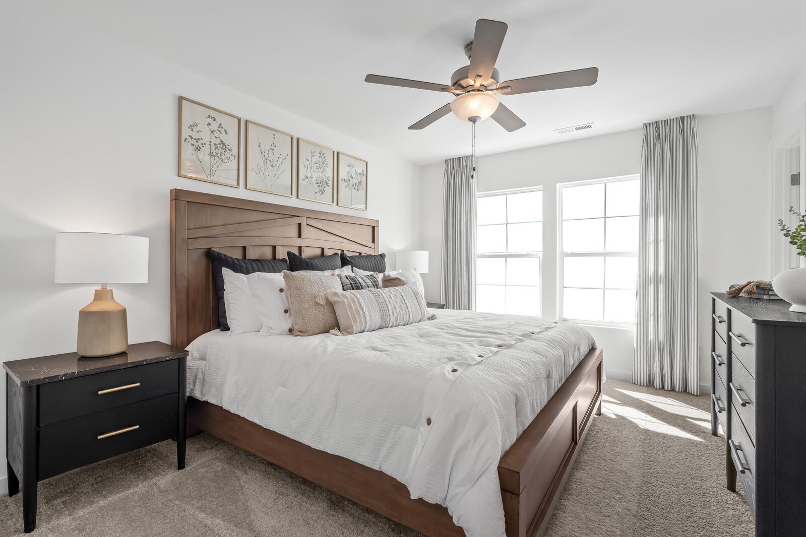 Primary bedroom at The Towns at Red River in Gallatin TN with wooden king bed, neutral bedding, ceiling fan, and large windows