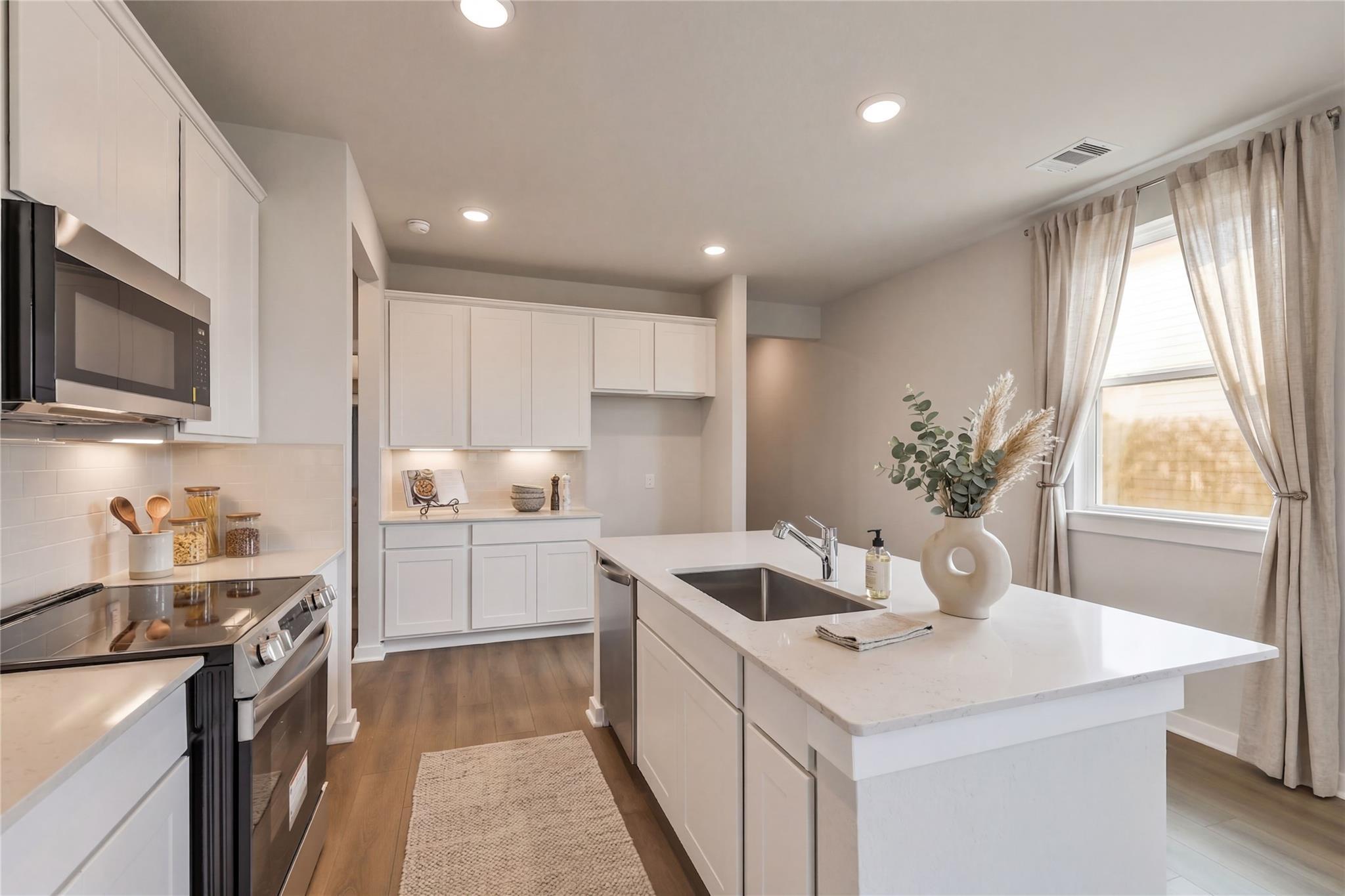 Modern white kitchen with central island, stainless steel appliances, and open layout in Davidson Homes The Frio G, Cleveland, Texas