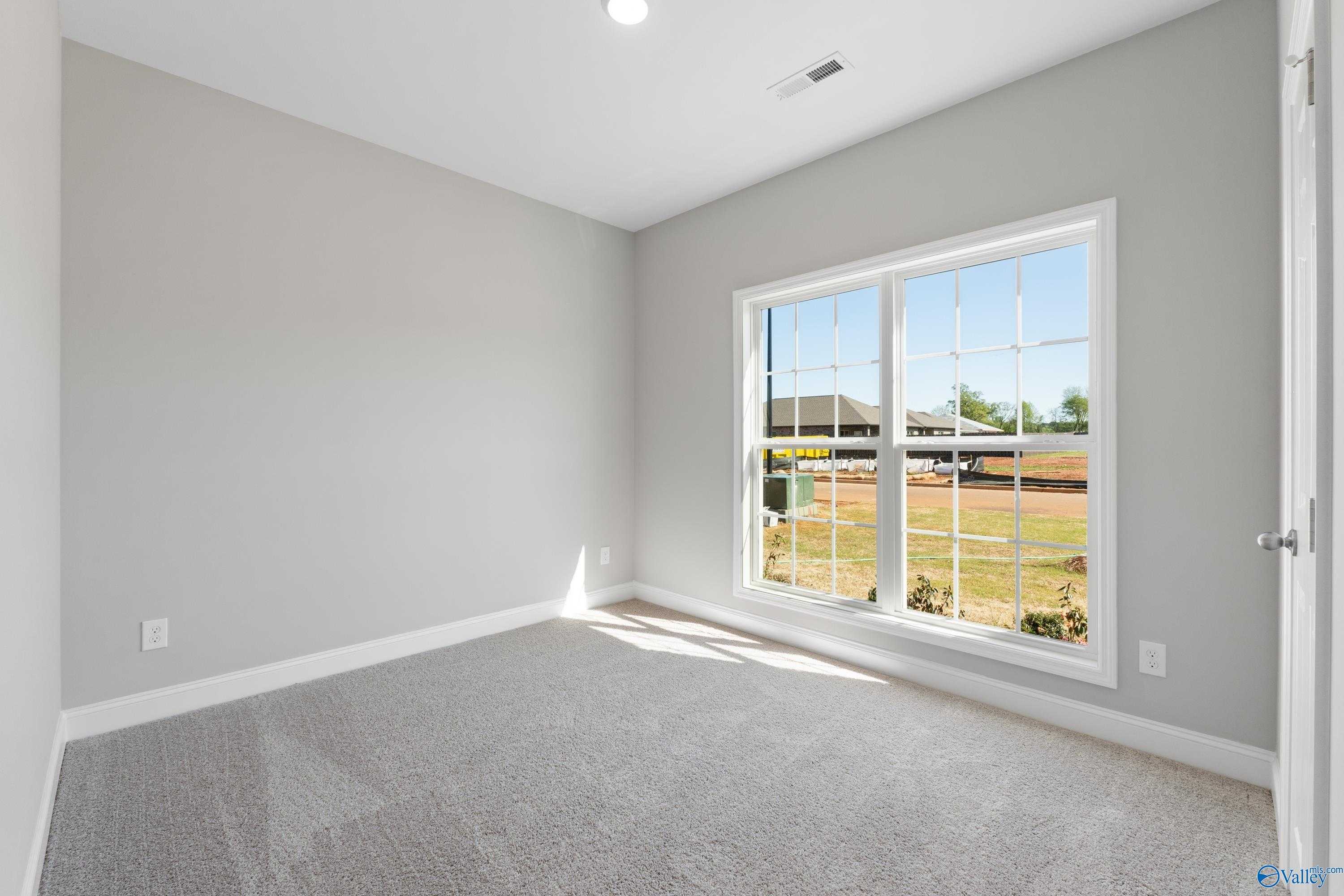 Bright secondary bedroom with gray walls, carpeted floor, and large window view of green yard in Davidson Homes The Asheville C, Athens, Alabama