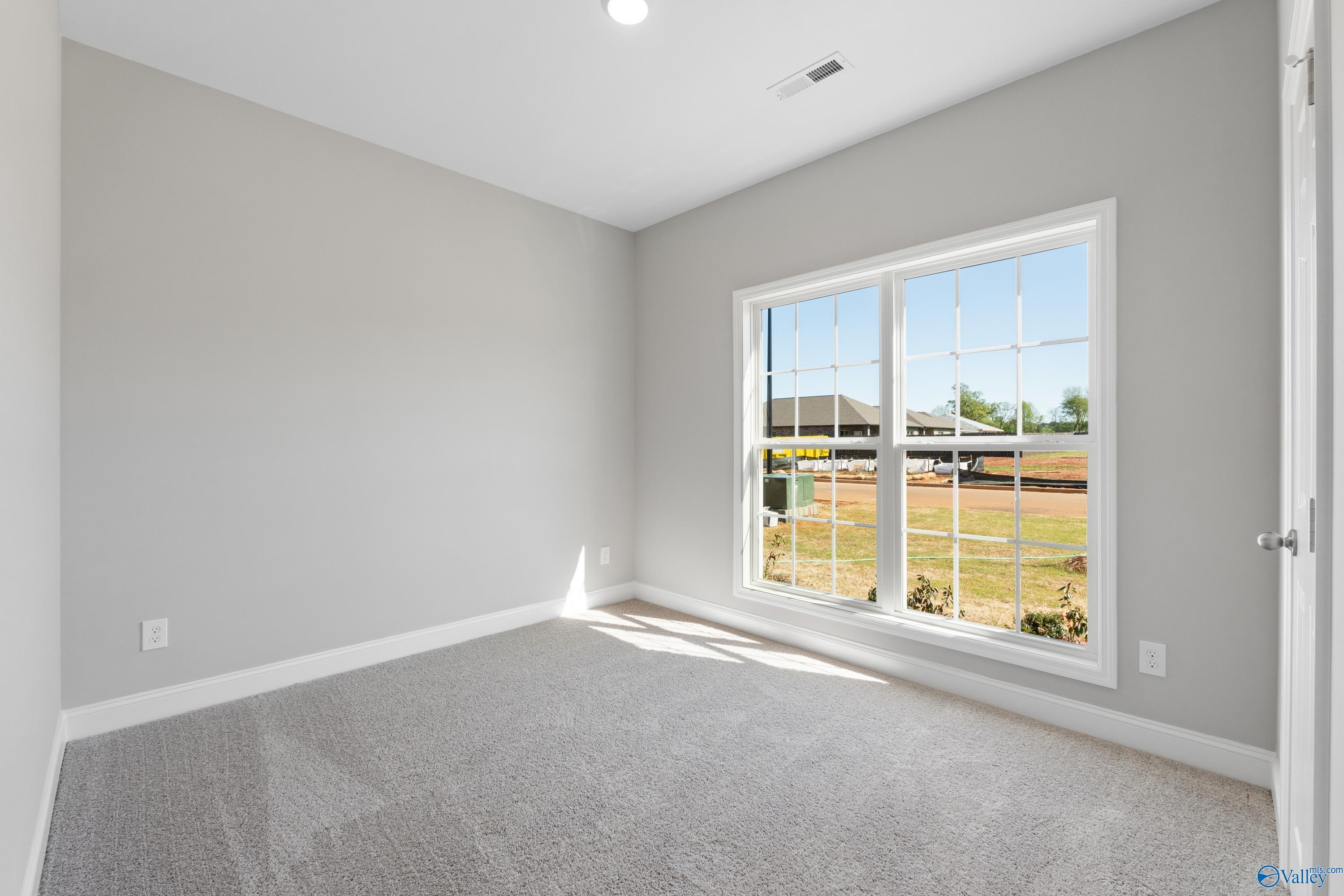Bright secondary bedroom with gray walls, carpeted floor, and large window view of green yard in Davidson Homes The Asheville C, Athens, Alabama
