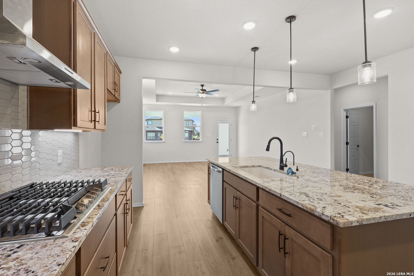 Kitchen island with granite countertops, pendant lights, and gas cooktop in Davidson Homes The Glenwood E, Comanche Ridge, San Antonio, Texas