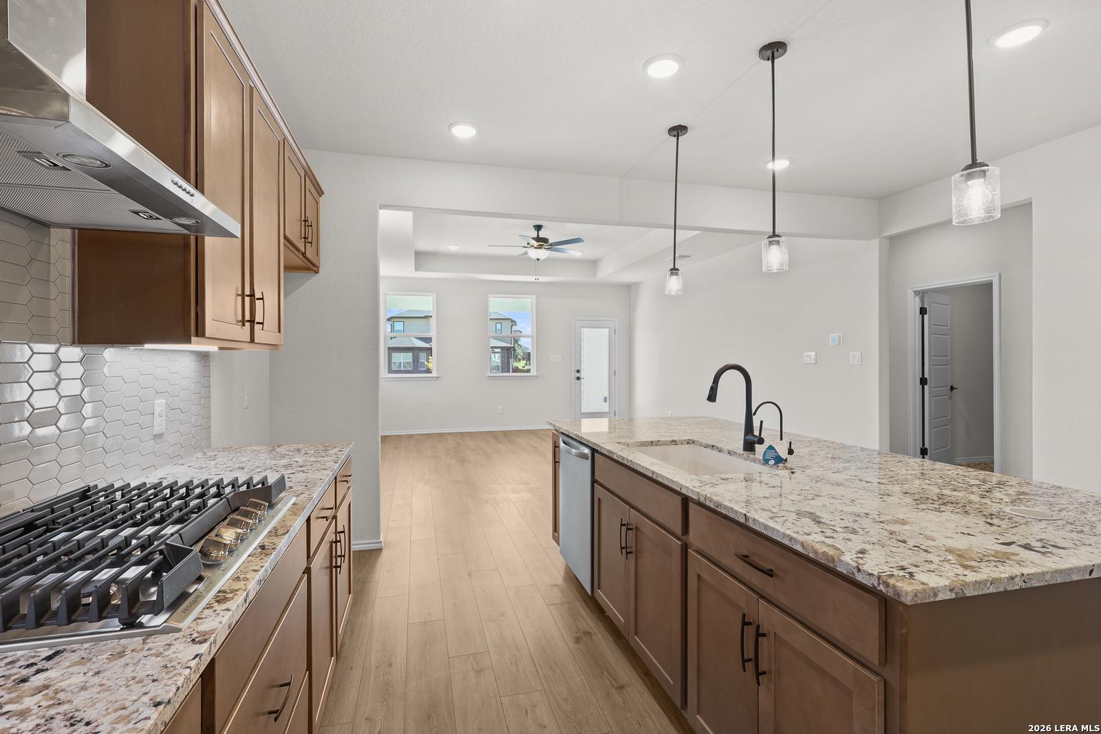 Kitchen island with granite countertops, pendant lights, and gas cooktop in Davidson Homes The Glenwood E, Comanche Ridge, San Antonio, Texas