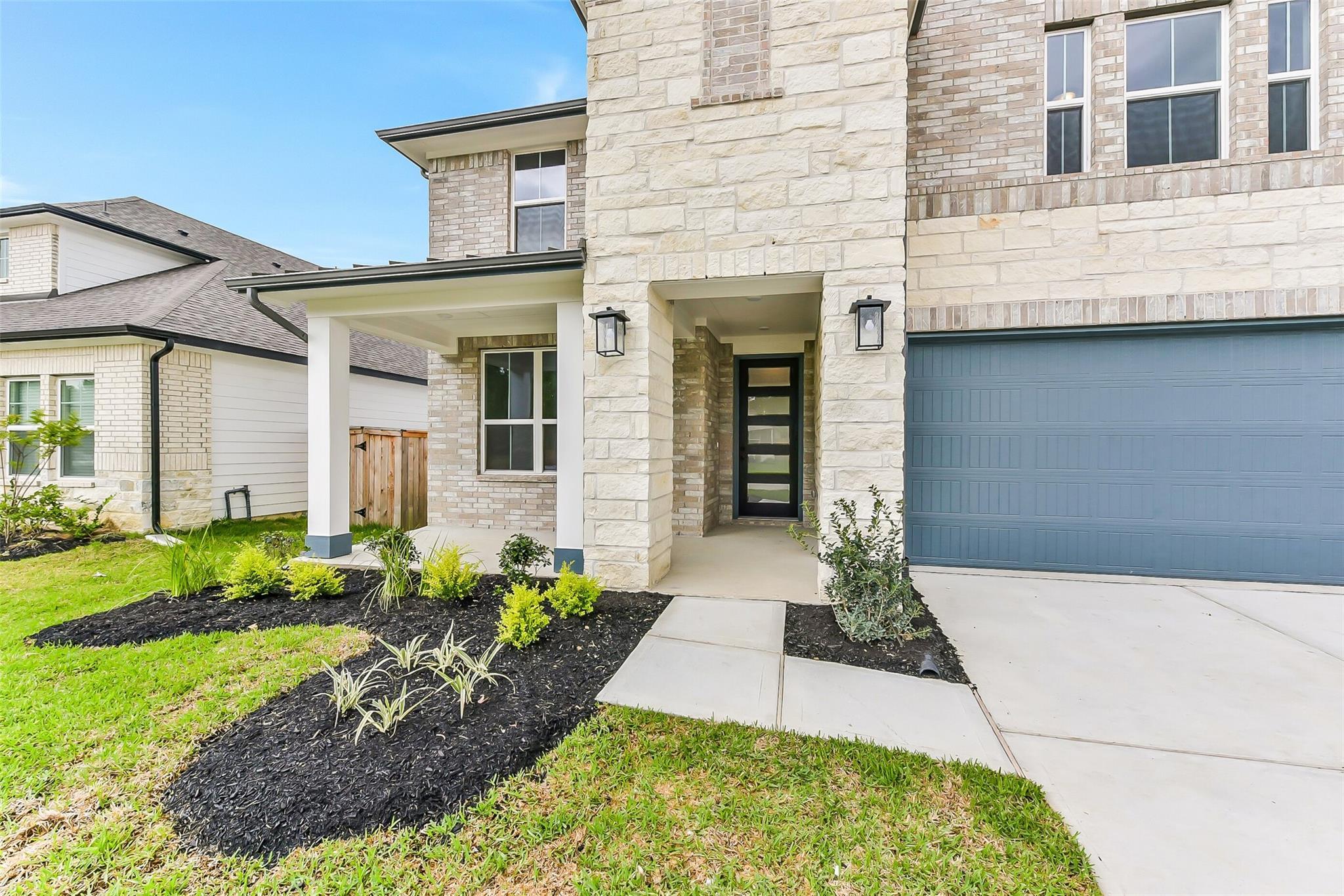 Modern two-story stone-brick home with covered porch, black door, two-car garage, landscaped yard in Sundance Cove, Crosby, Texas