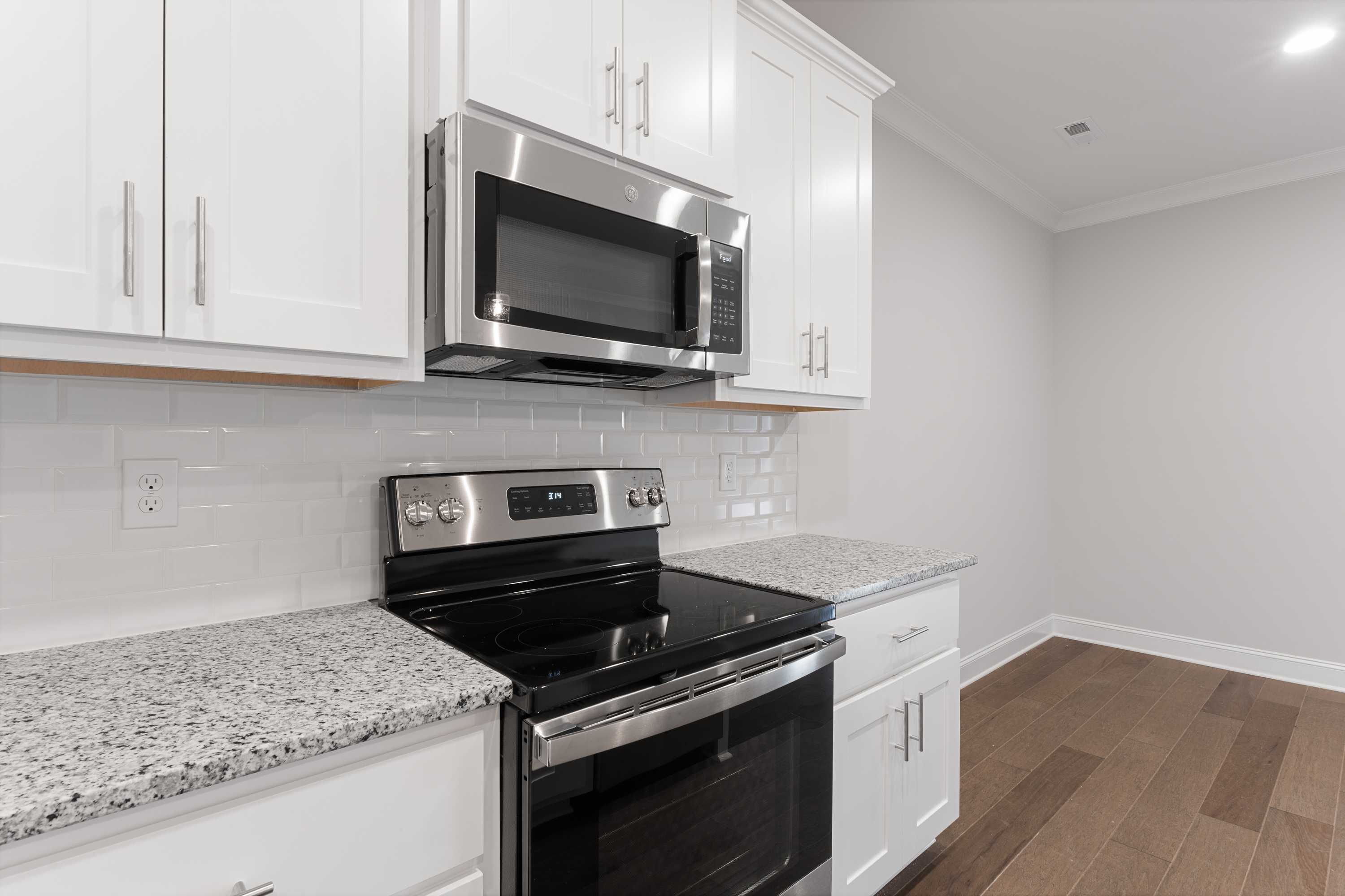 Modern kitchen in The Copeland C with white shaker cabinets, stainless steel microwave and range, granite counters, subway tile backsplash