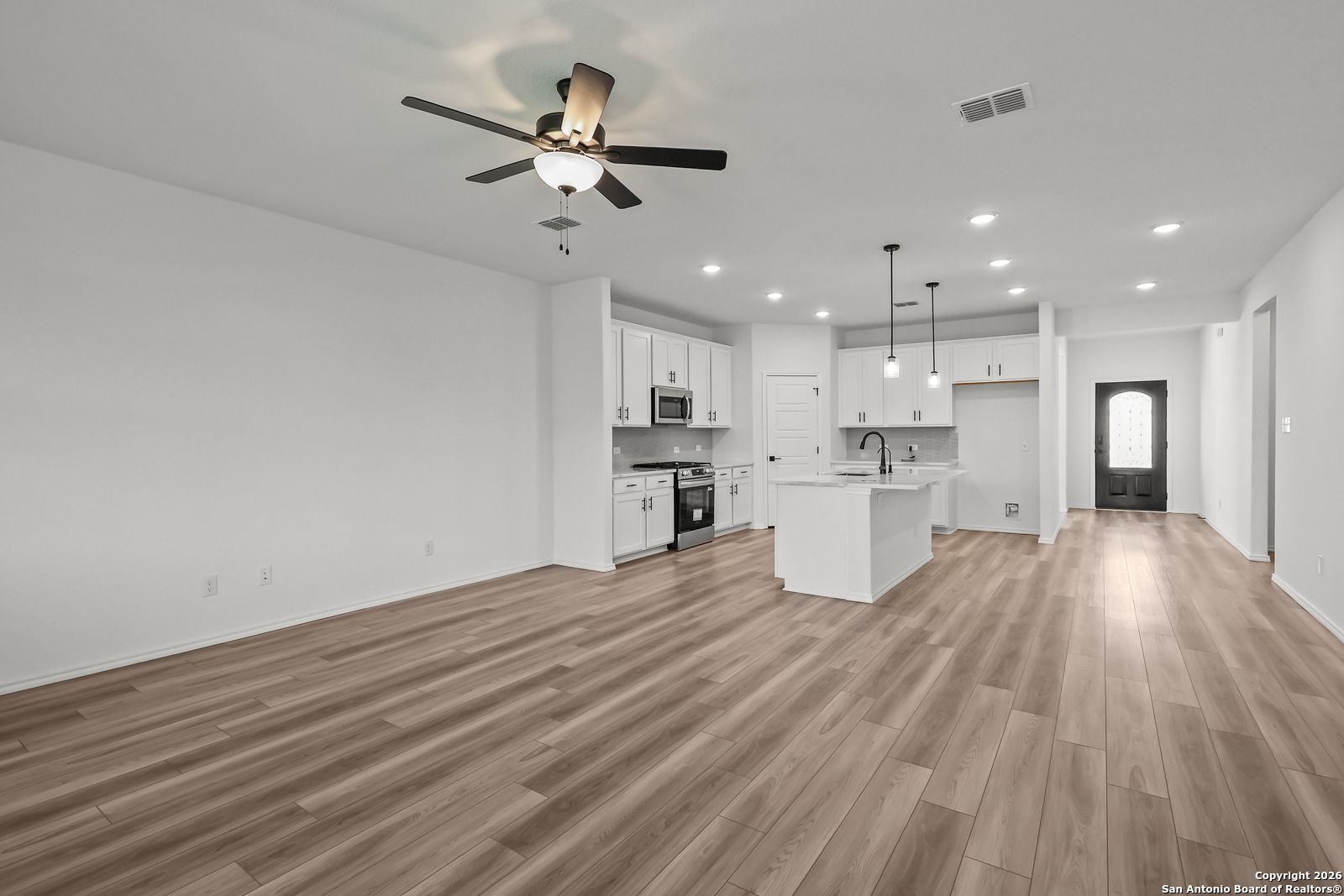 Modern open kitchen with white cabinets, central island sink, stainless appliances, and hardwood floors in Davidson Homes The Douglas E, San Antonio