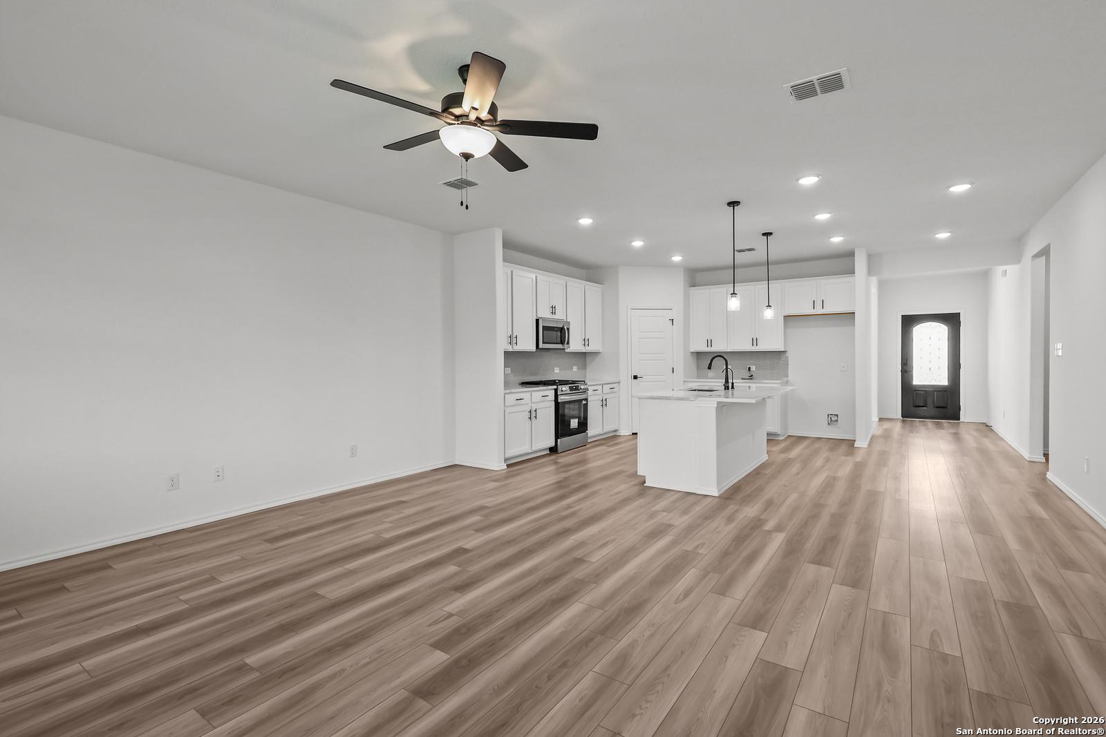 Modern open kitchen with white cabinets, central island sink, stainless appliances, and hardwood floors in Davidson Homes The Douglas E, San Antonio