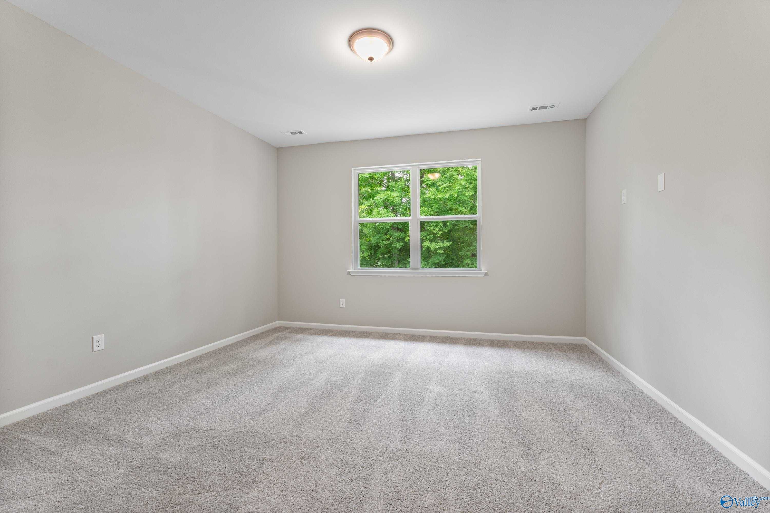 Bright empty bedroom with neutral gray walls, plush carpet, and large window overlooking green trees in The Aurora 4-bedroom home, Fayetteville TN