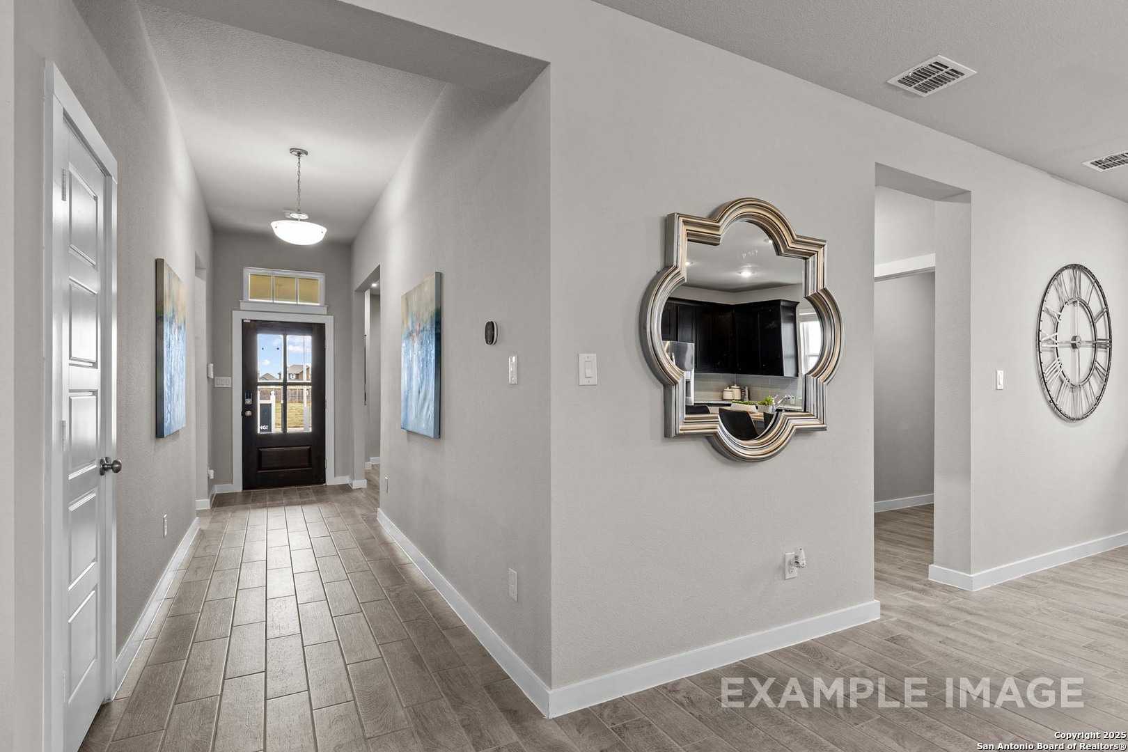 Elegant foyer hallway with light wood floors, ornate mirror TV, wall clock, and front door in The Collin B home, Seguin, Texas