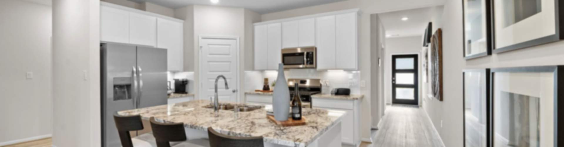 Spacious modern kitchen in new Cleveland home with white cabinets, granite island, stainless appliances, bar stools, hardwood floors