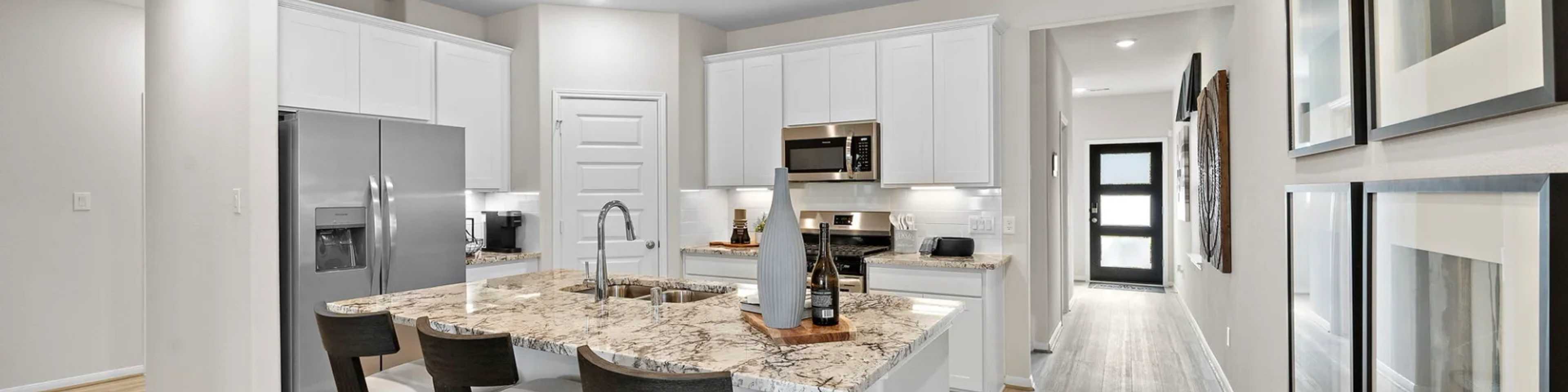 Spacious modern kitchen in new Cleveland home with white cabinets, granite island, stainless appliances, bar stools, hardwood floors