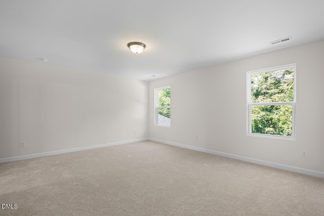 Bright bedroom with carpet flooring and large windows overlooking trees in Davidson Homes Willow B plan, Zebulon NC