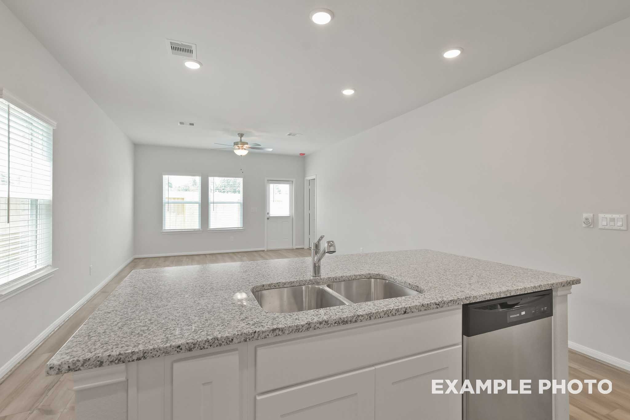 Modern open-concept kitchen in The Comal floor plan with granite island, double sink, stainless dishwasher, white cabinets, and recessed lighting