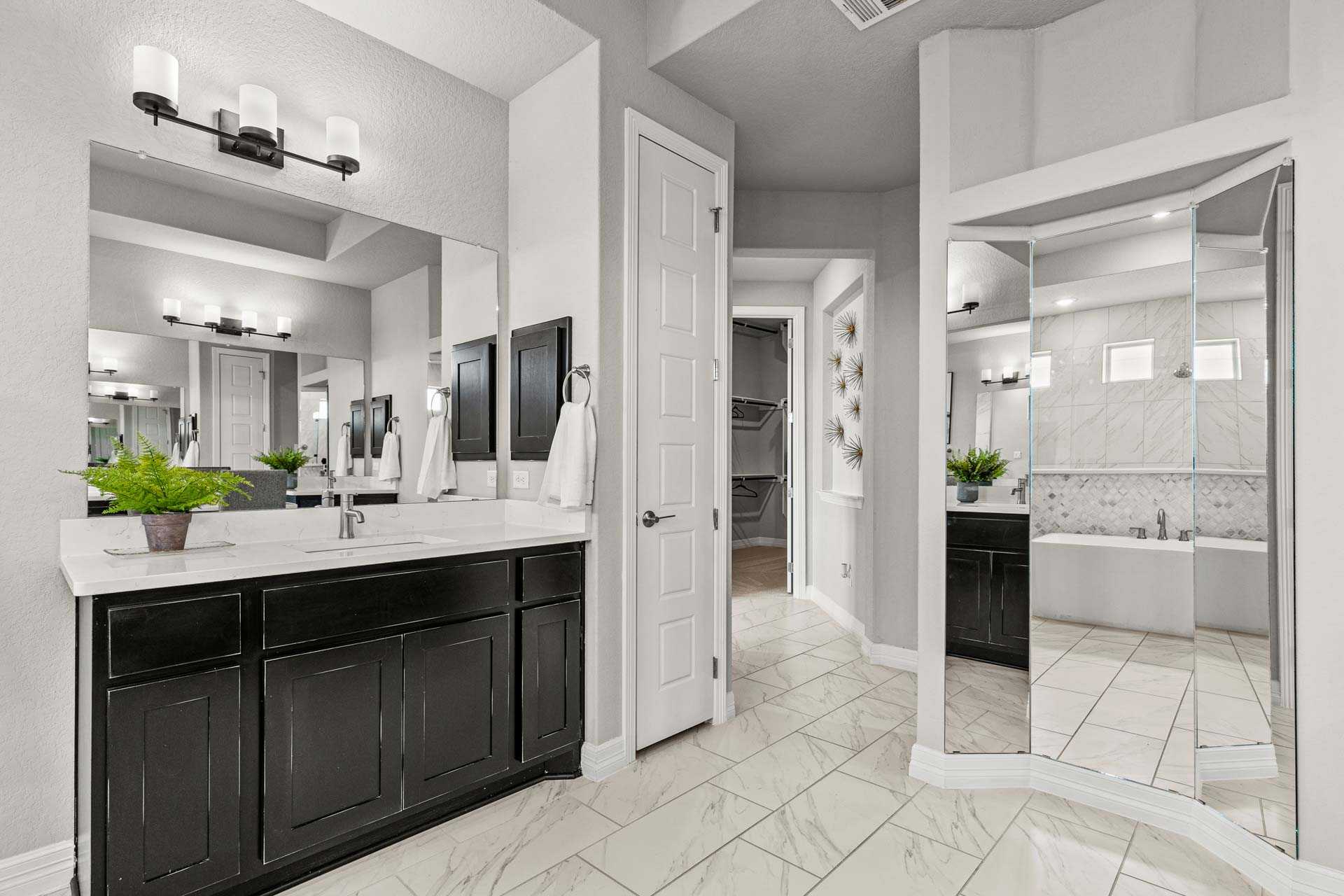 Spacious master bathroom in The Summerlin B with dual black vanities, freestanding tub, large mirrors, and plants