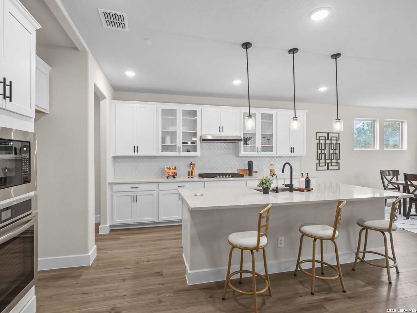 Modern white kitchen with quartz island, pendant lights, and stainless appliances in The Belmont H home, Potranco Oaks.