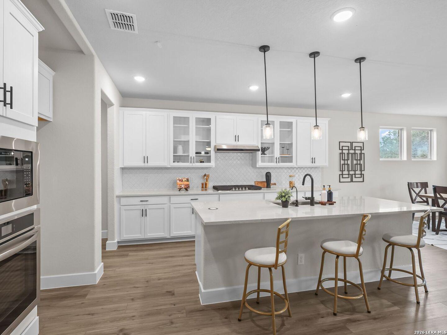 Modern white kitchen with quartz island, pendant lights, and stainless appliances in The Belmont H home, Potranco Oaks.