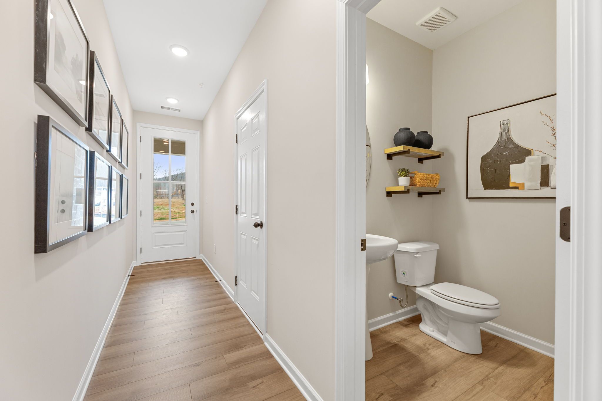 Hallway and powder room in Hemingway community Cumming GA home with light wood floors, modern artwork, and sleek black accents