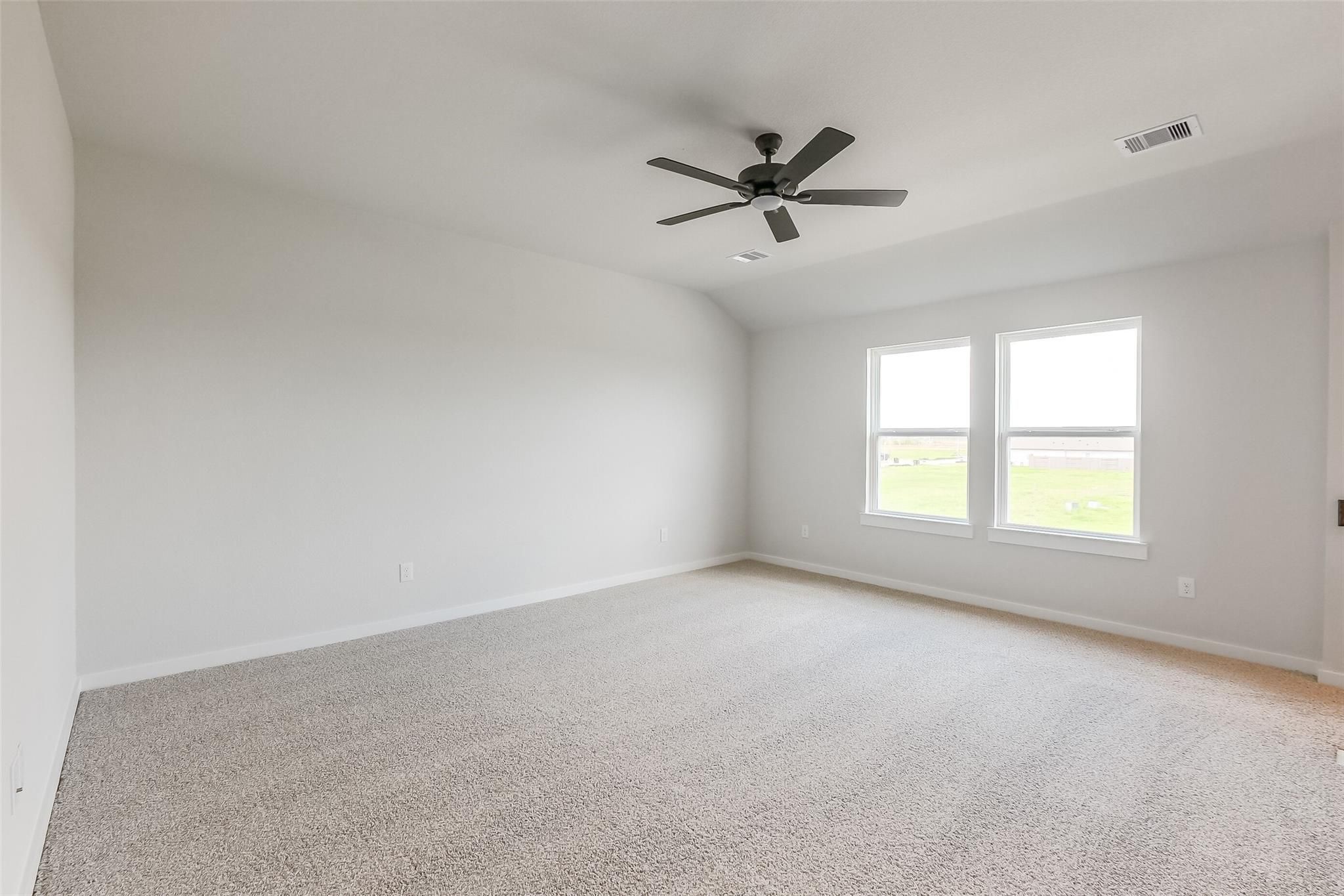 Bright secondary bedroom with ceiling fan, beige walls, and windows overlooking fields in Davidson Homes The Tierra B, Beasley, Texas