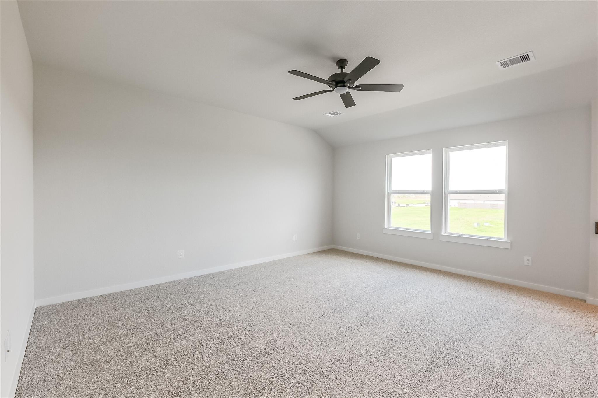 Bright secondary bedroom with ceiling fan, beige walls, and windows overlooking fields in Davidson Homes The Tierra B, Beasley, Texas