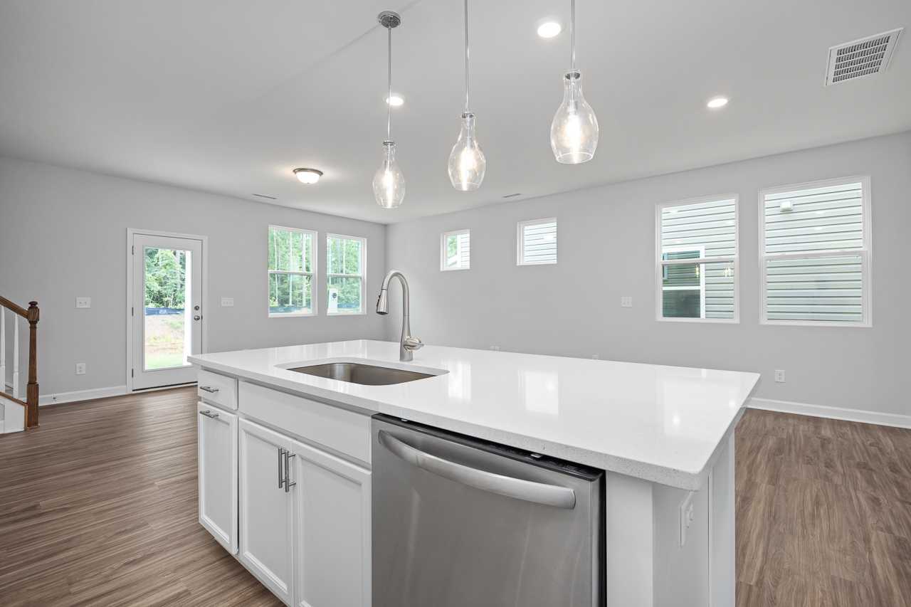 Modern kitchen in The Durham D featuring white quartz island, stainless steel sink and dishwasher, pendant lights, hardwood floors