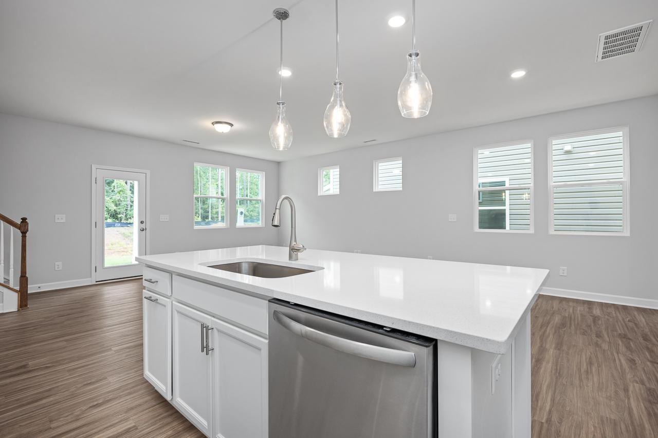 Bright open kitchen in The Durham C with white island, stainless dishwasher, pendant lights, and large windows