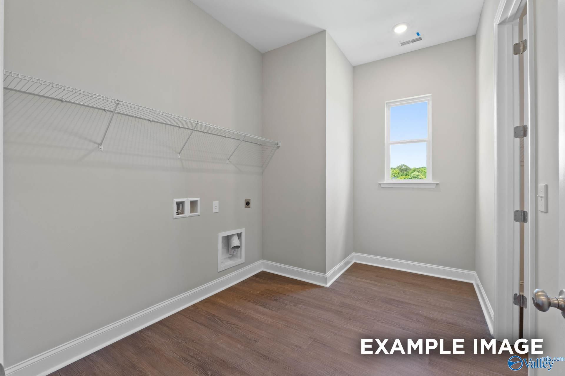 Spacious laundry room with wire shelving, gray walls, hardwood floors, and window in Evermore Homes The Arcadia, Owens Cross Roads, Alabama