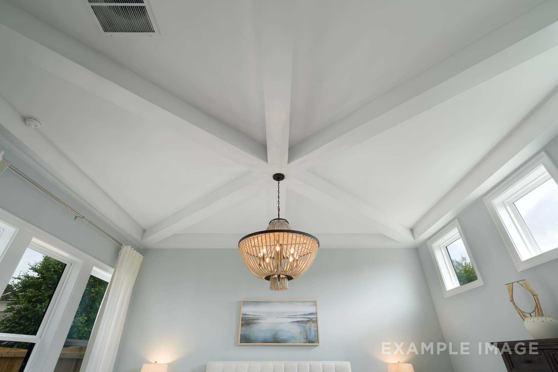 Spacious master bedroom in The Seaside with vaulted beamed ceiling, beaded chandelier, and serene seascape art