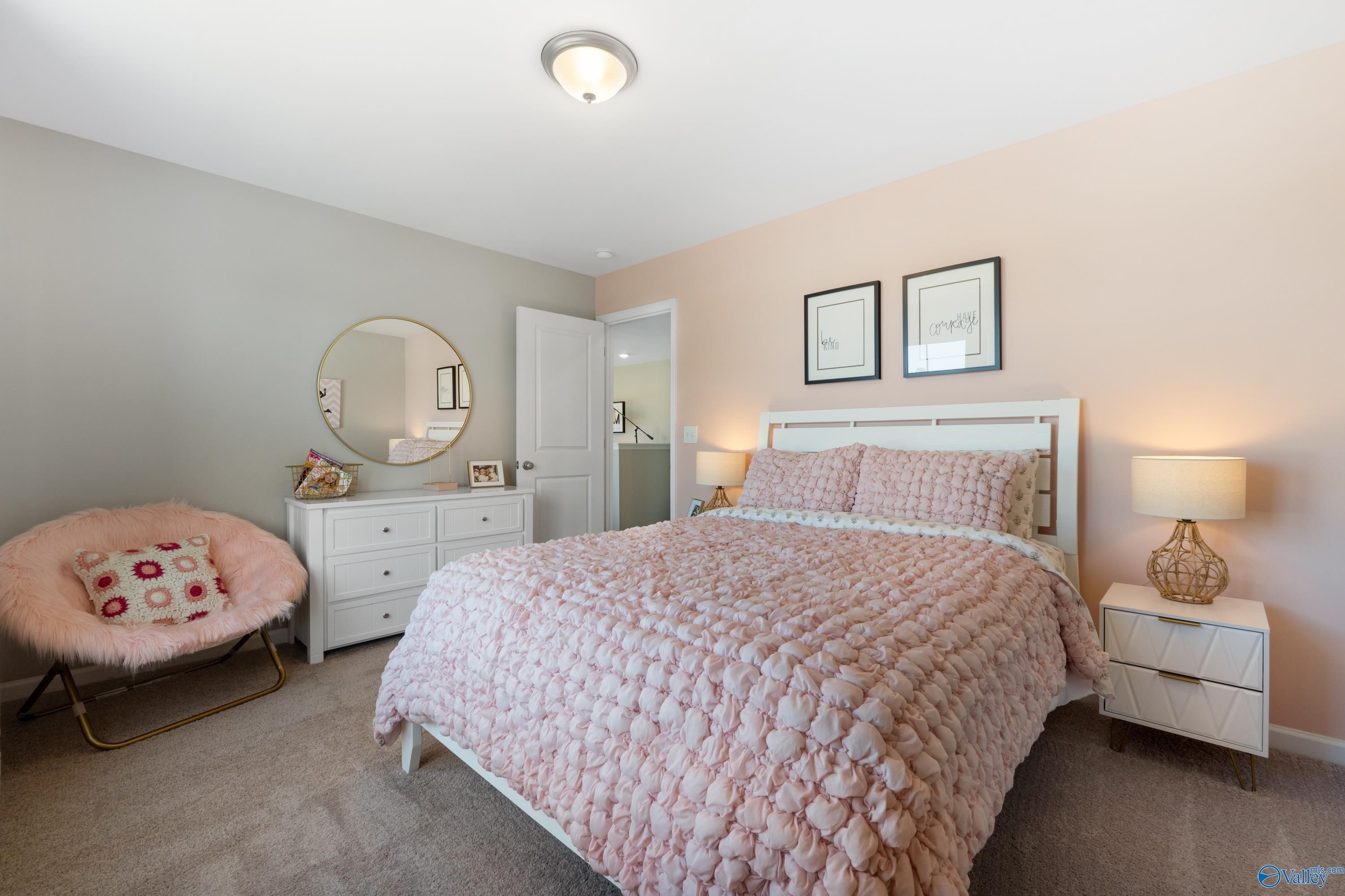 Charming pink bedroom with textured queen bed, fluffy accent chair, gold mirror, white dresser in Davidson Homes The Stella, Madison Alabama