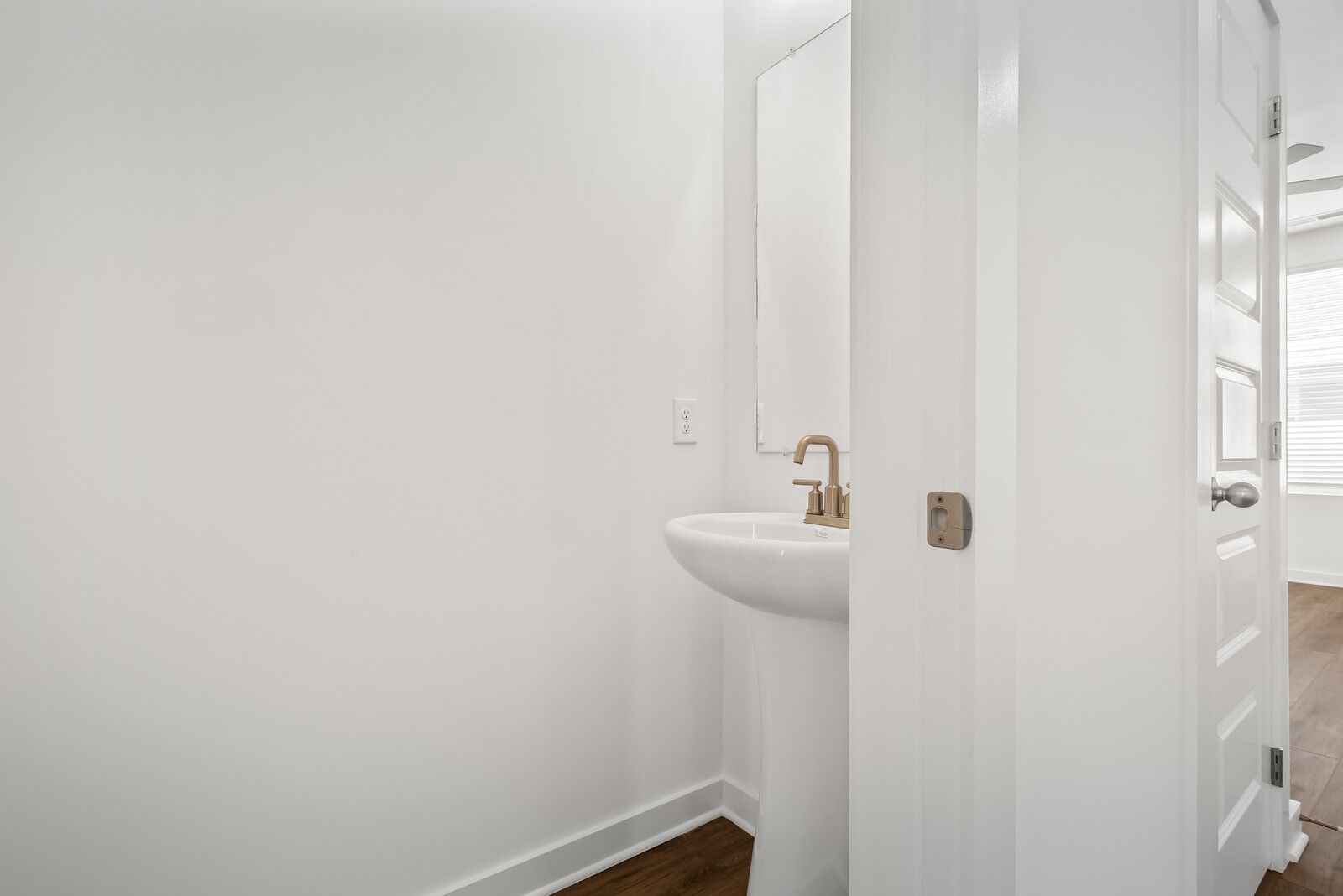 Modern powder room with white pedestal sink, gold faucet, and mirror in Davidson Homes The Gordon C, White House, TN