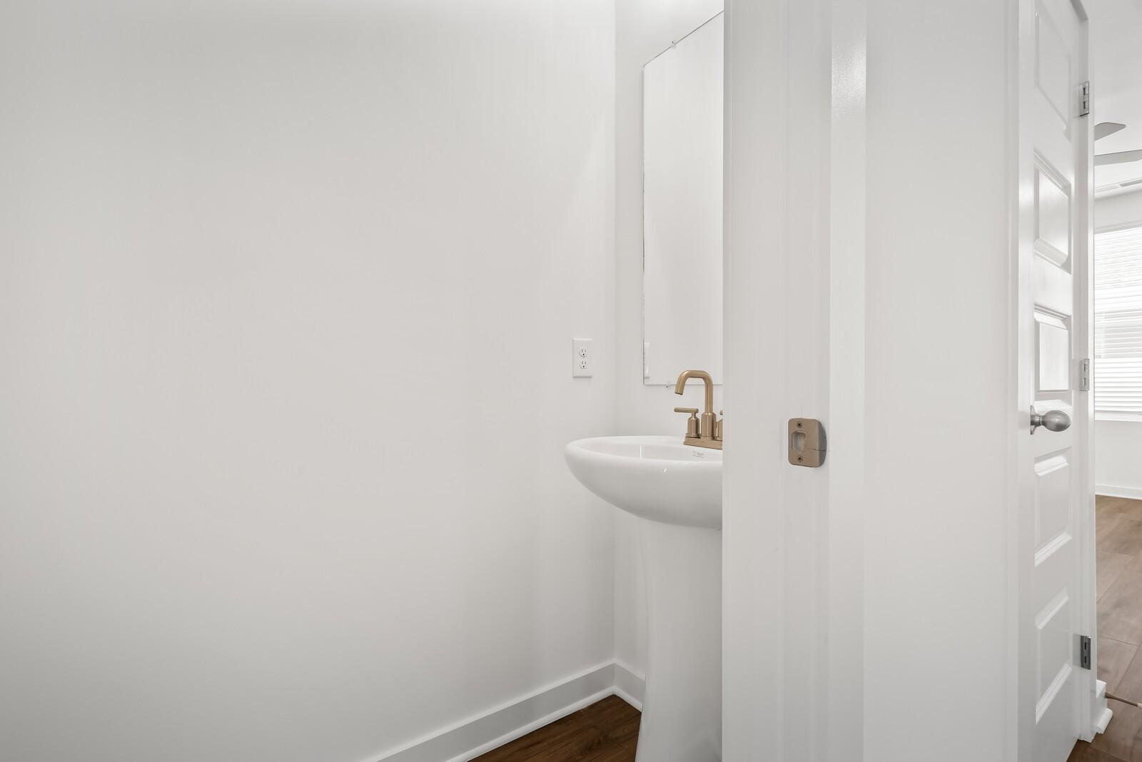 Modern powder room with white pedestal sink, gold faucet, and mirror in Davidson Homes The Gordon C, White House, TN