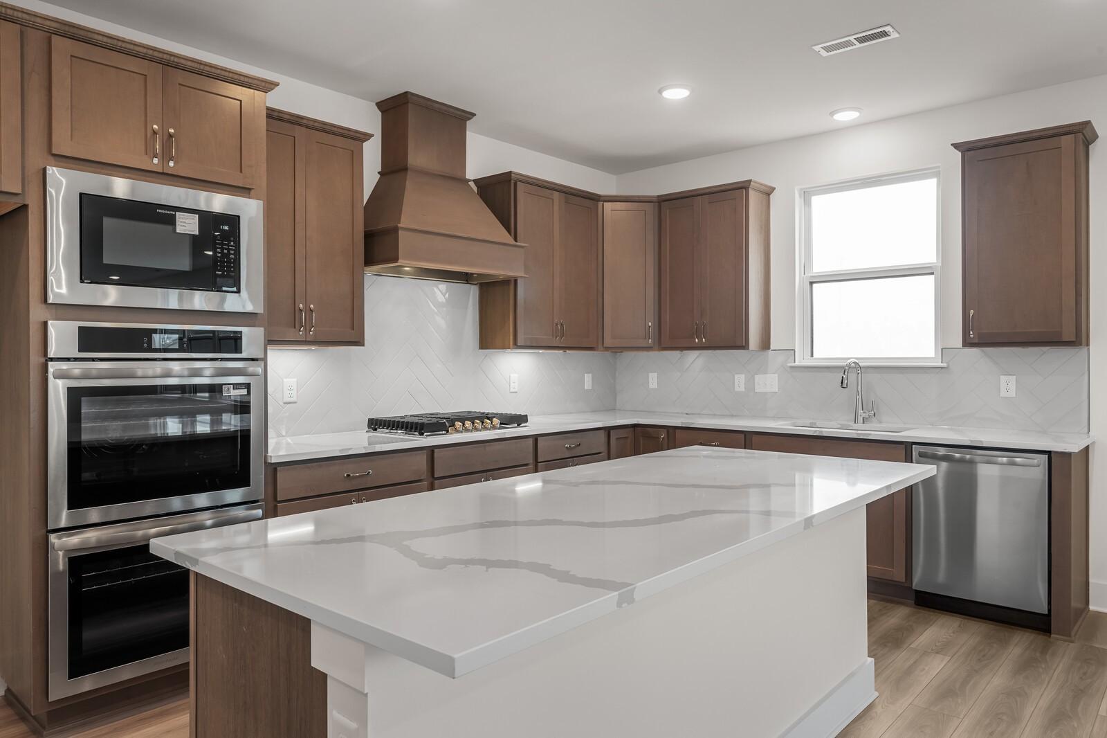 Modern kitchen with quartz island, stainless appliances, and wood cabinets in The Henry C floor plan, Benders Cove home.