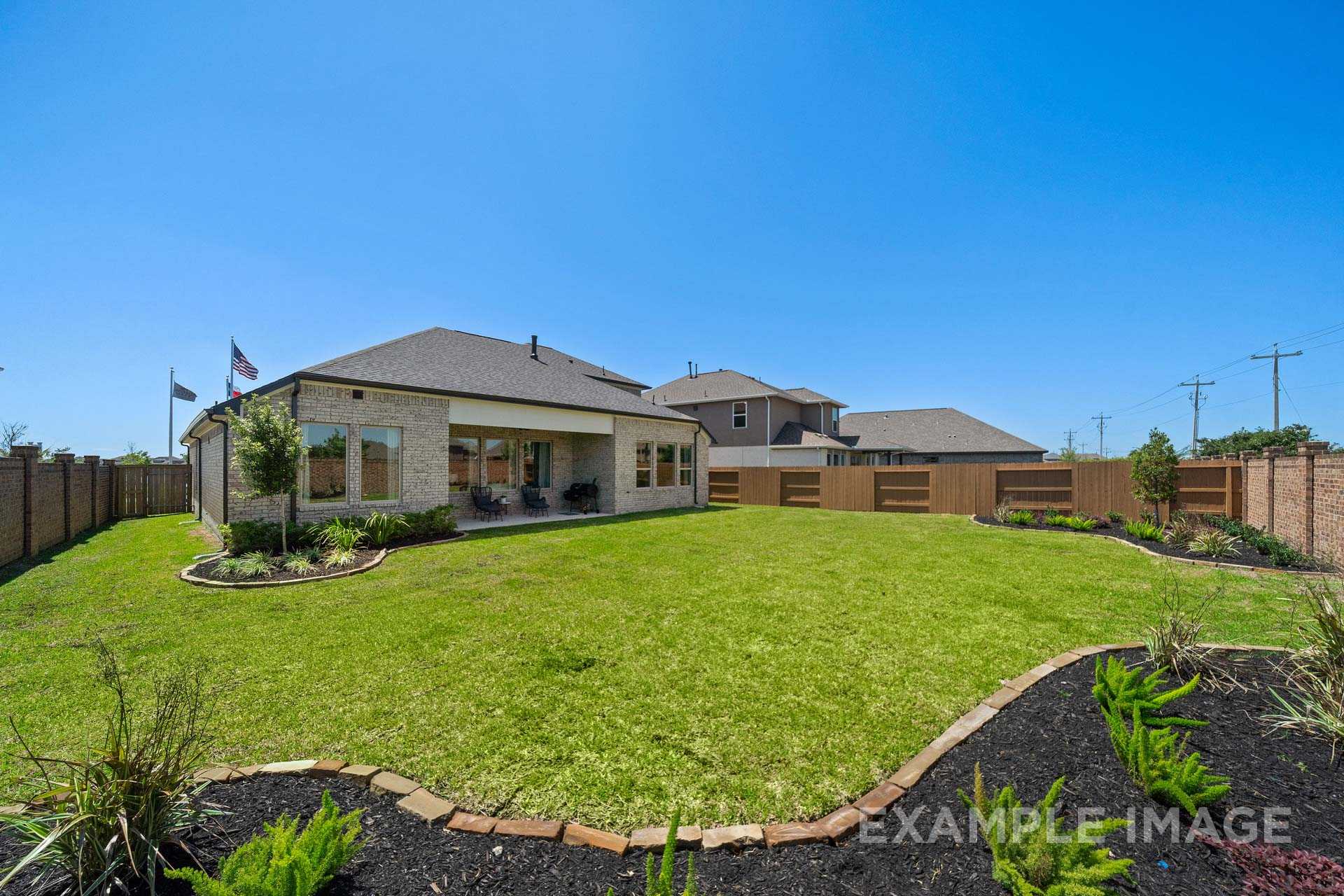 Backyard view of The Edward C single-story home featuring 3-car garage, lush green lawn, and wooden fence in Texas City