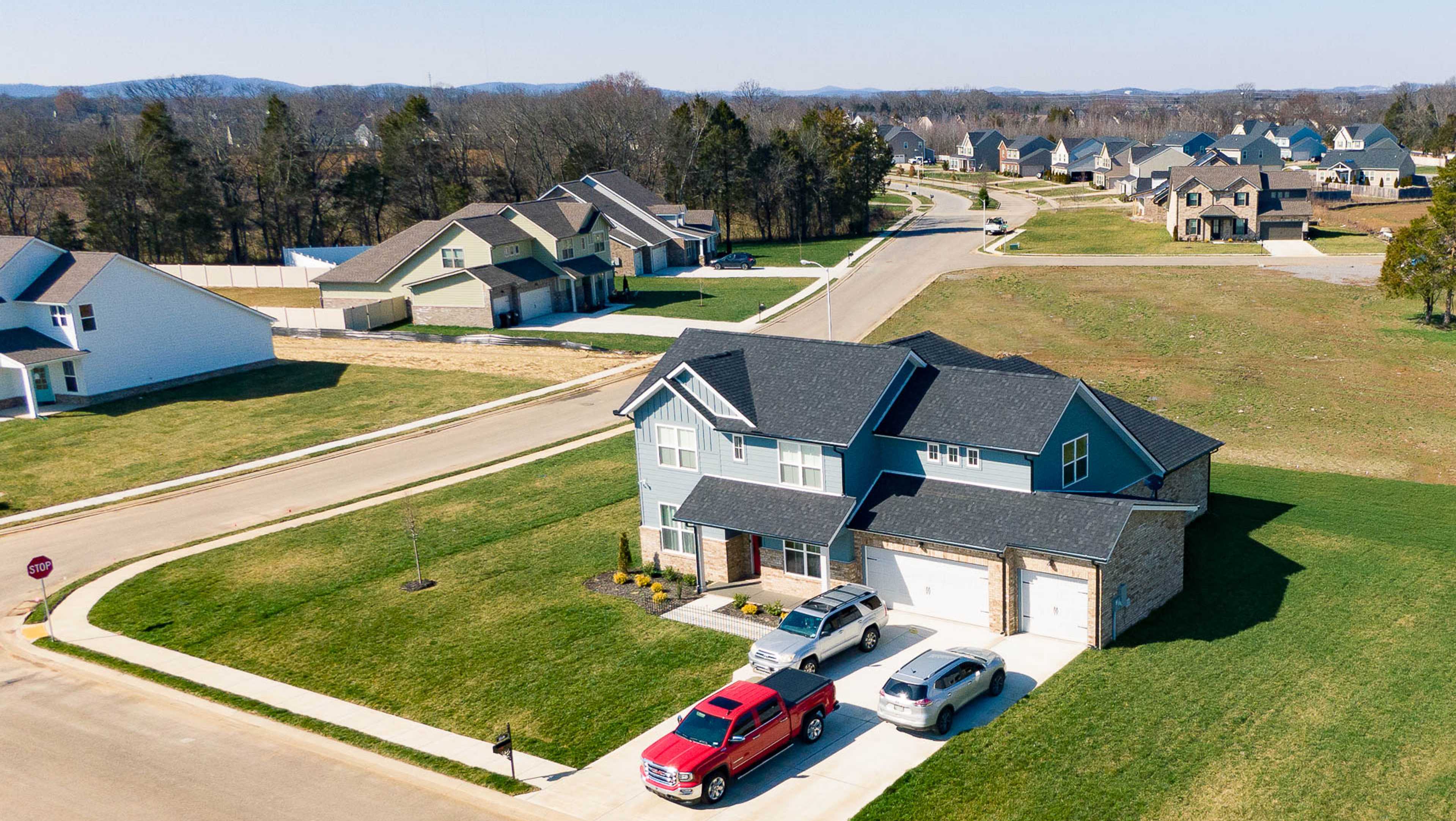 Aerial view of modern Davidson Homes Nashville neighborhood, two-story house with gray siding, garage, red truck, and lush green lawns