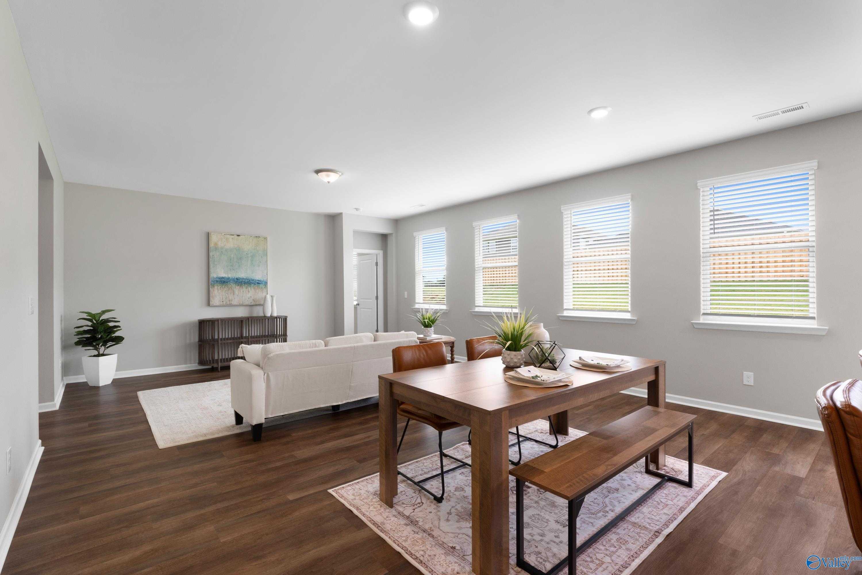 Open-concept living-dining area with beige sofa, wooden table, benches, plants, large windows in The Noble 3-bedroom home, Madison, Alabama