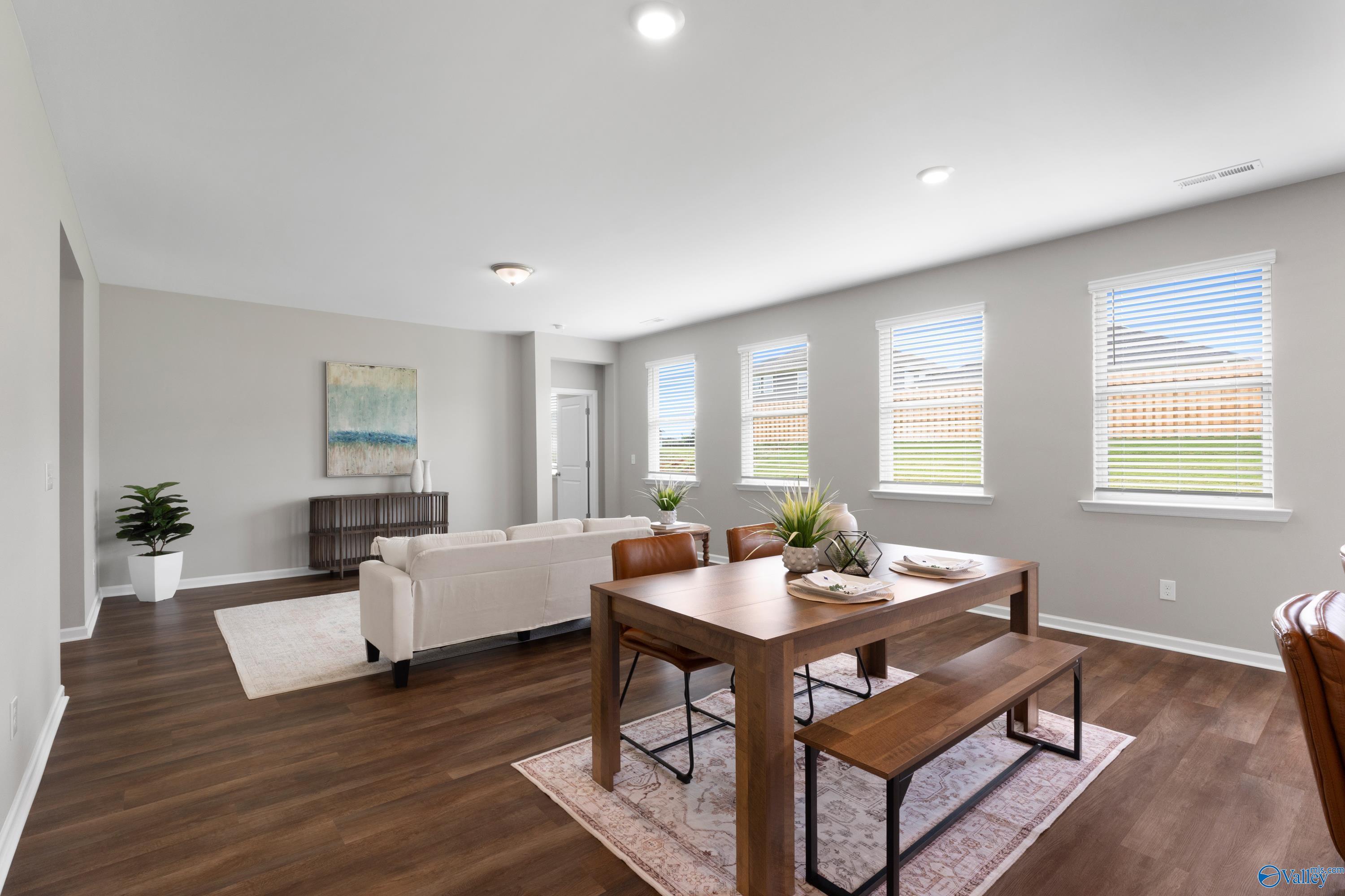 Open-concept living and dining area with large windows, beige sofa, wooden table, and plants in The Noble 3-bedroom home, Madison, Alabama