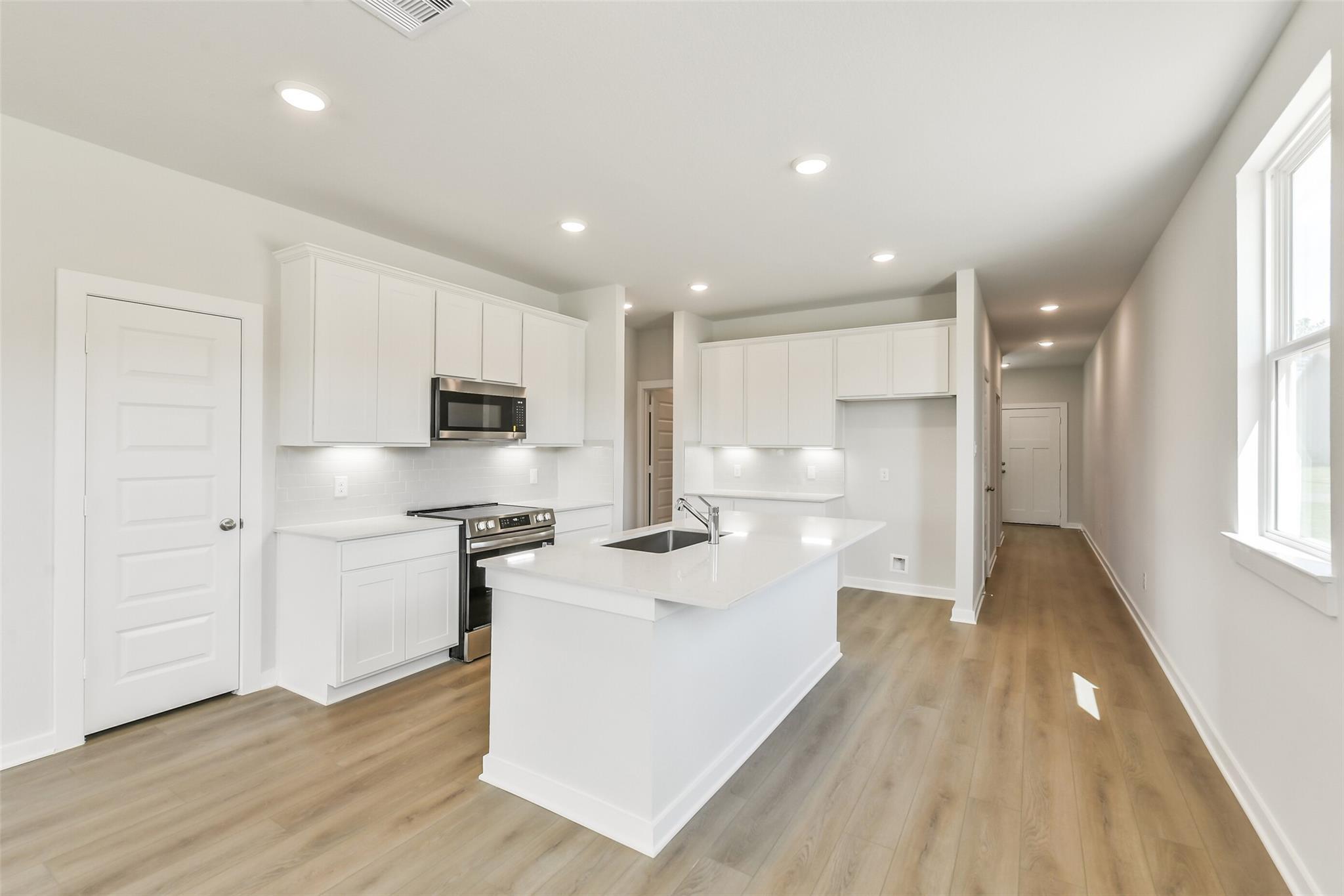 Bright white kitchen with quartz island sink, stainless appliances, and open layout in Davidson Homes The Frio G, Conroe TX