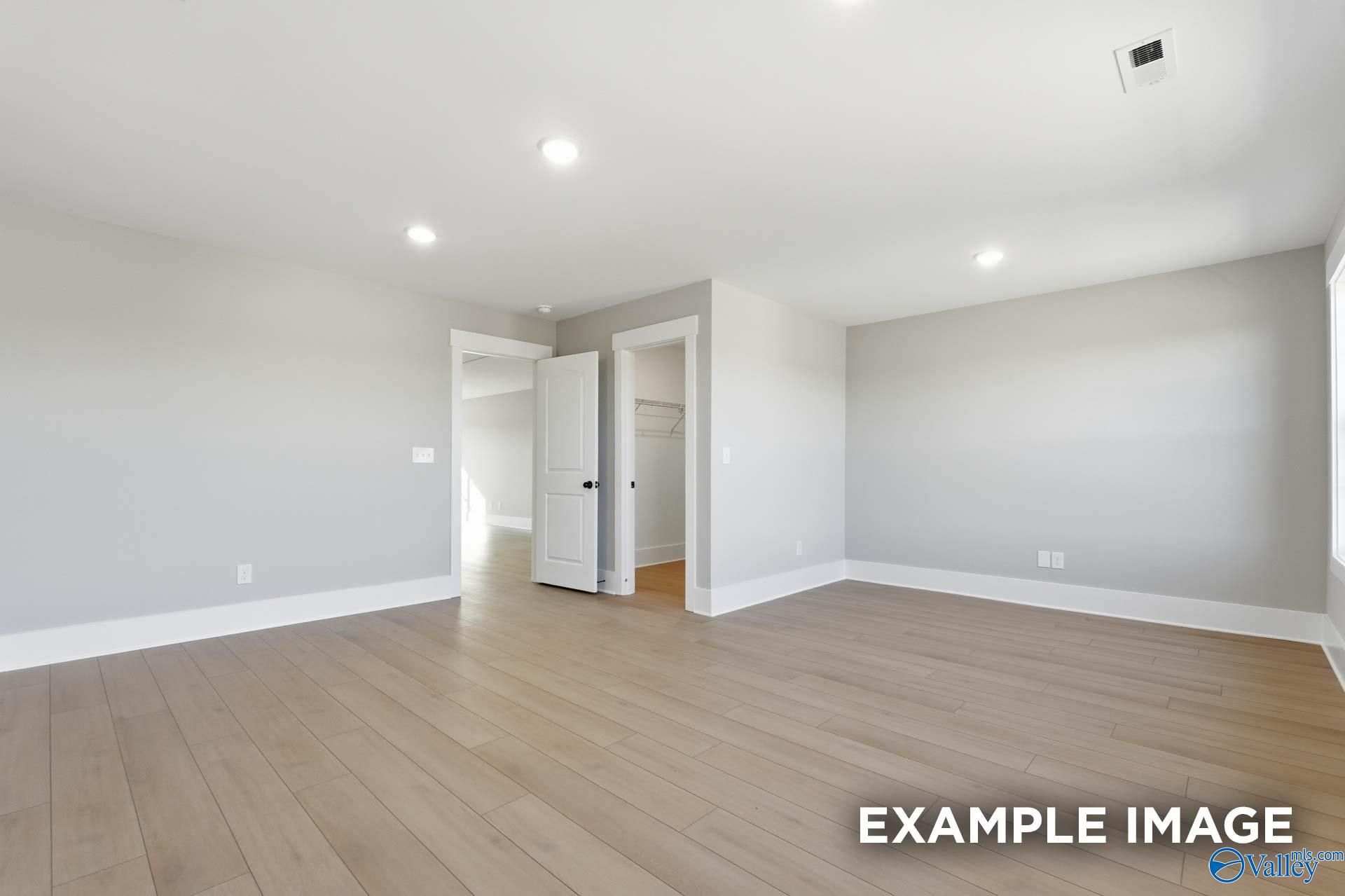 Spacious empty bedroom with light oak hardwood floors, gray walls, and double doors in Davidson Homes The Emory, Decatur, Alabama
